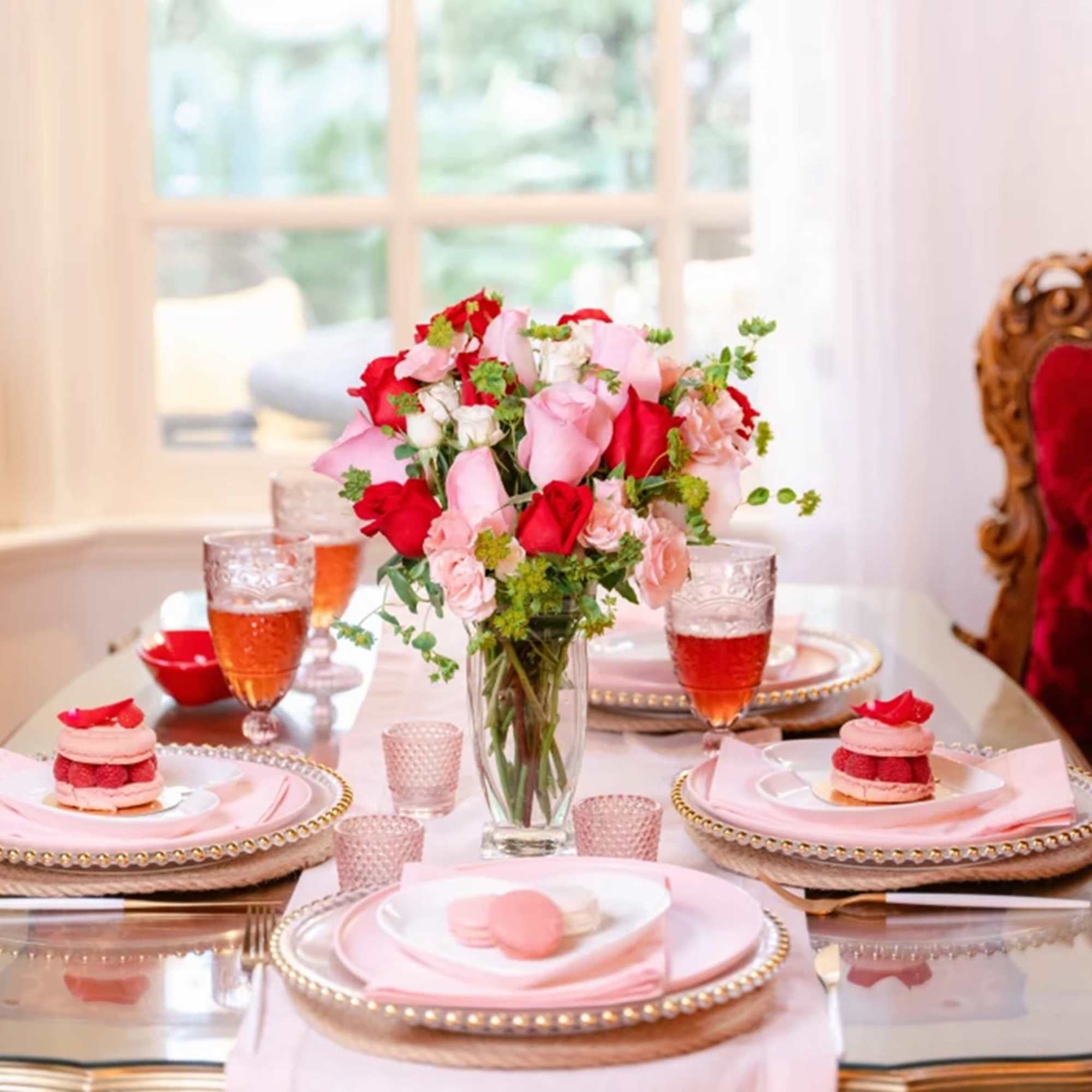 Pink and red rose bouquet in a clear glass vase on a set dining table.
