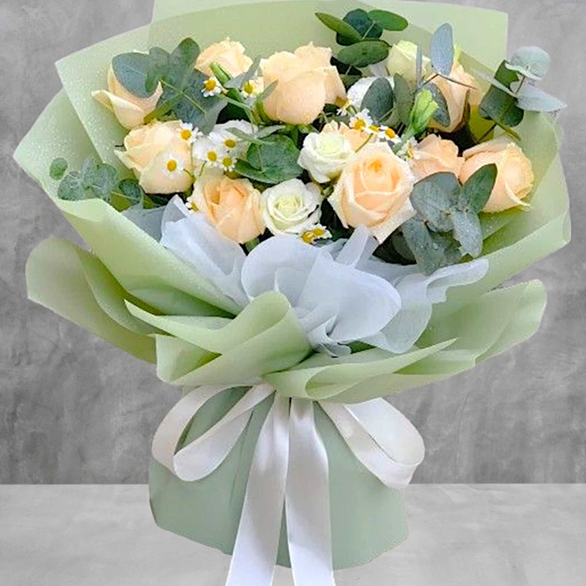Bouquet of pale peach roses with white filler flowers and eucalyptus, wrapped in green paper