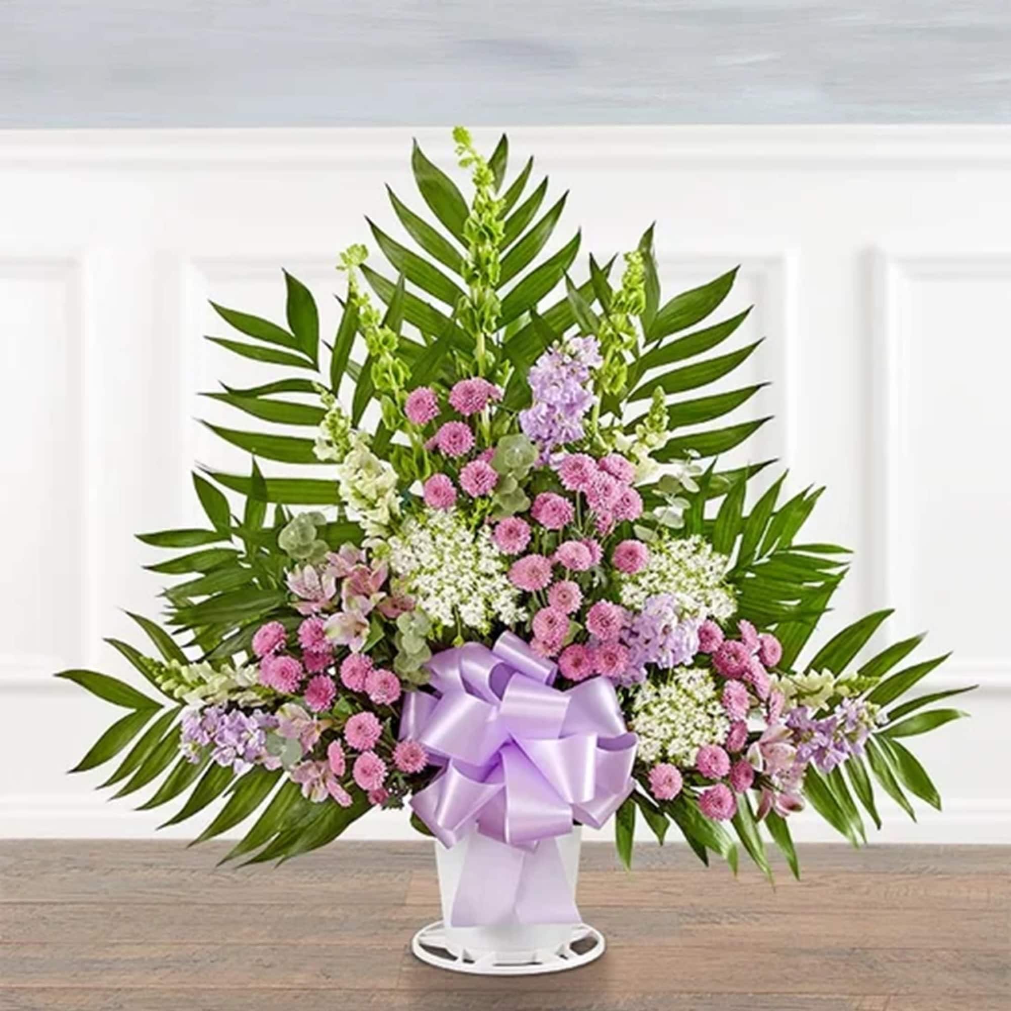 Standing floral spray with pink and lavender blooms in a white vase with a purple bow