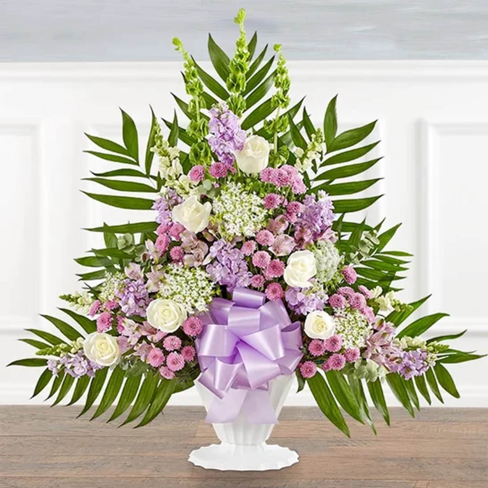 Lavender and white floral arrangement in a white urn with a purple bow