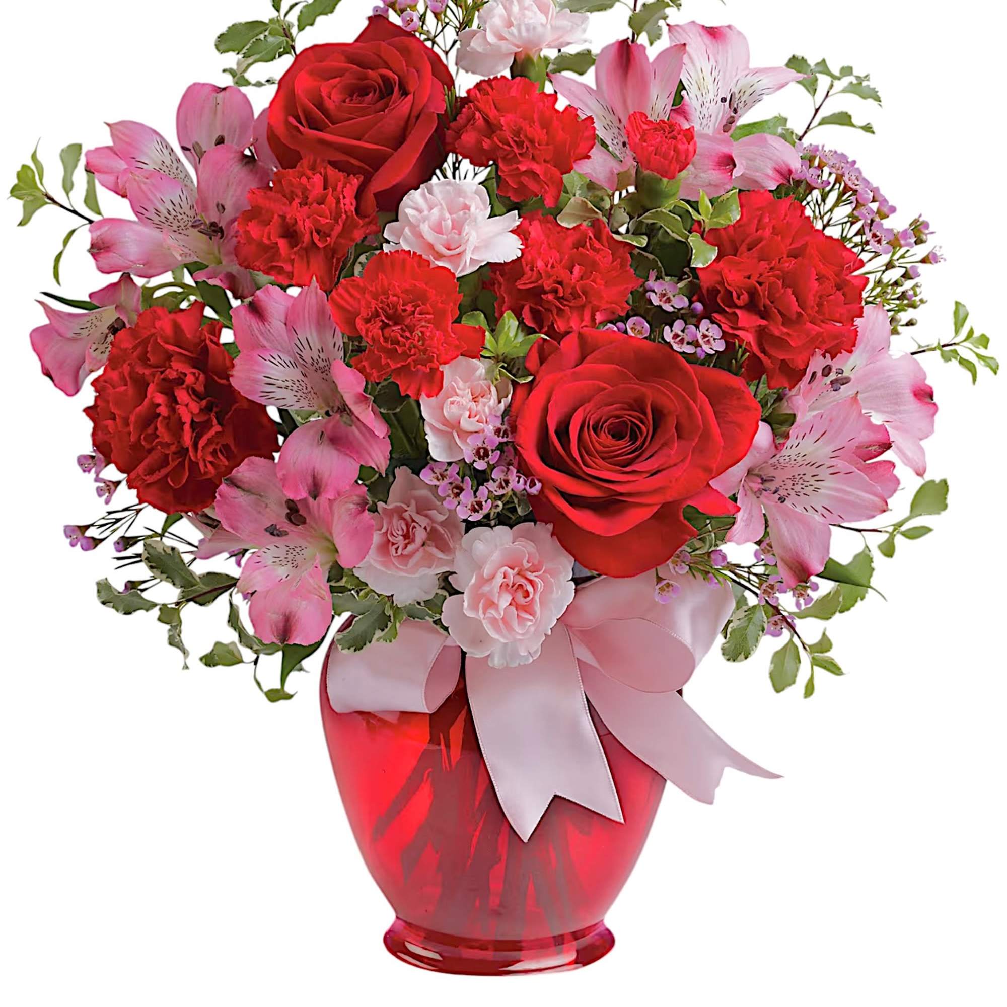Red roses and pink flowers arranged in a red vase with a ribbon
