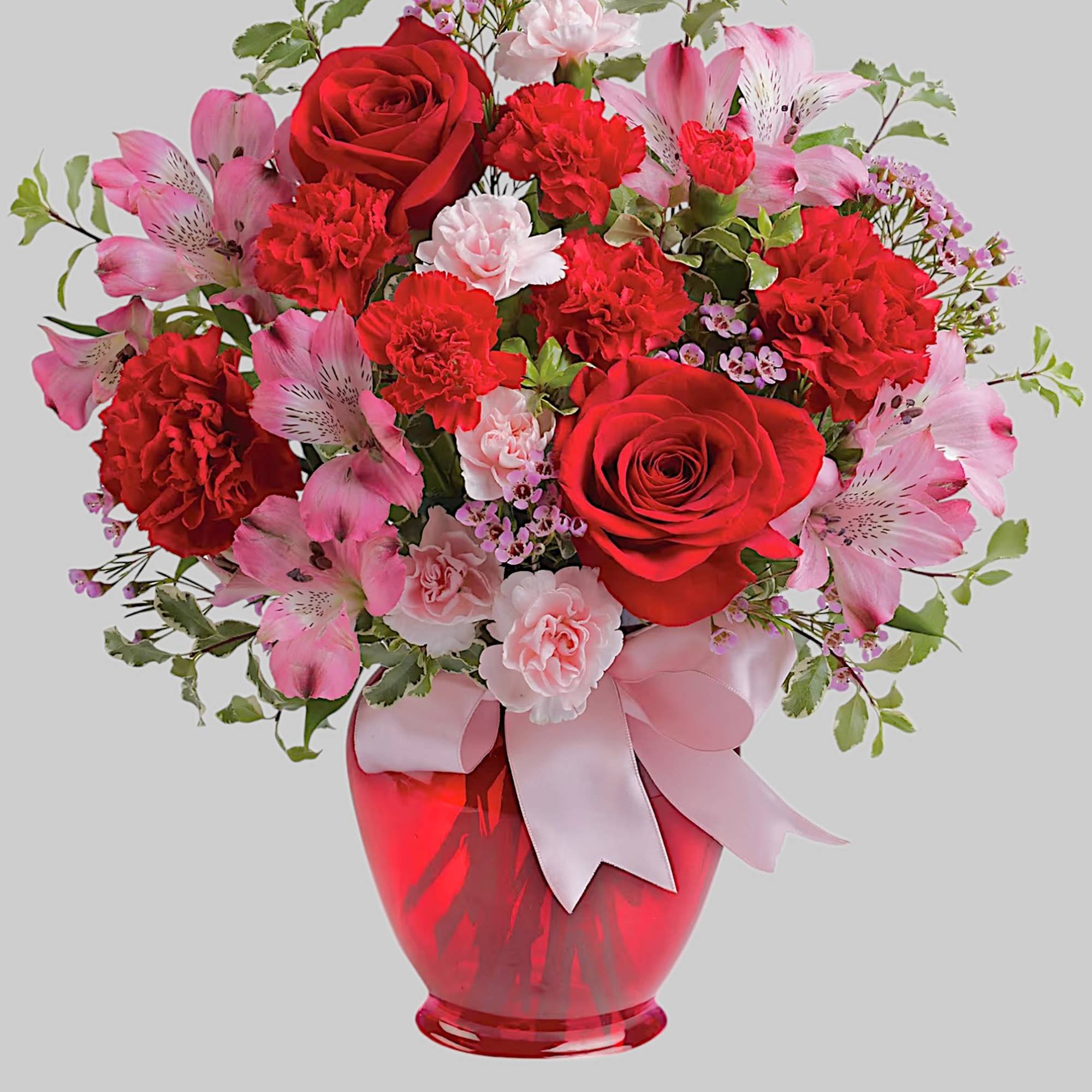 Red and pink bouquet in a red glass vase with a ribbon