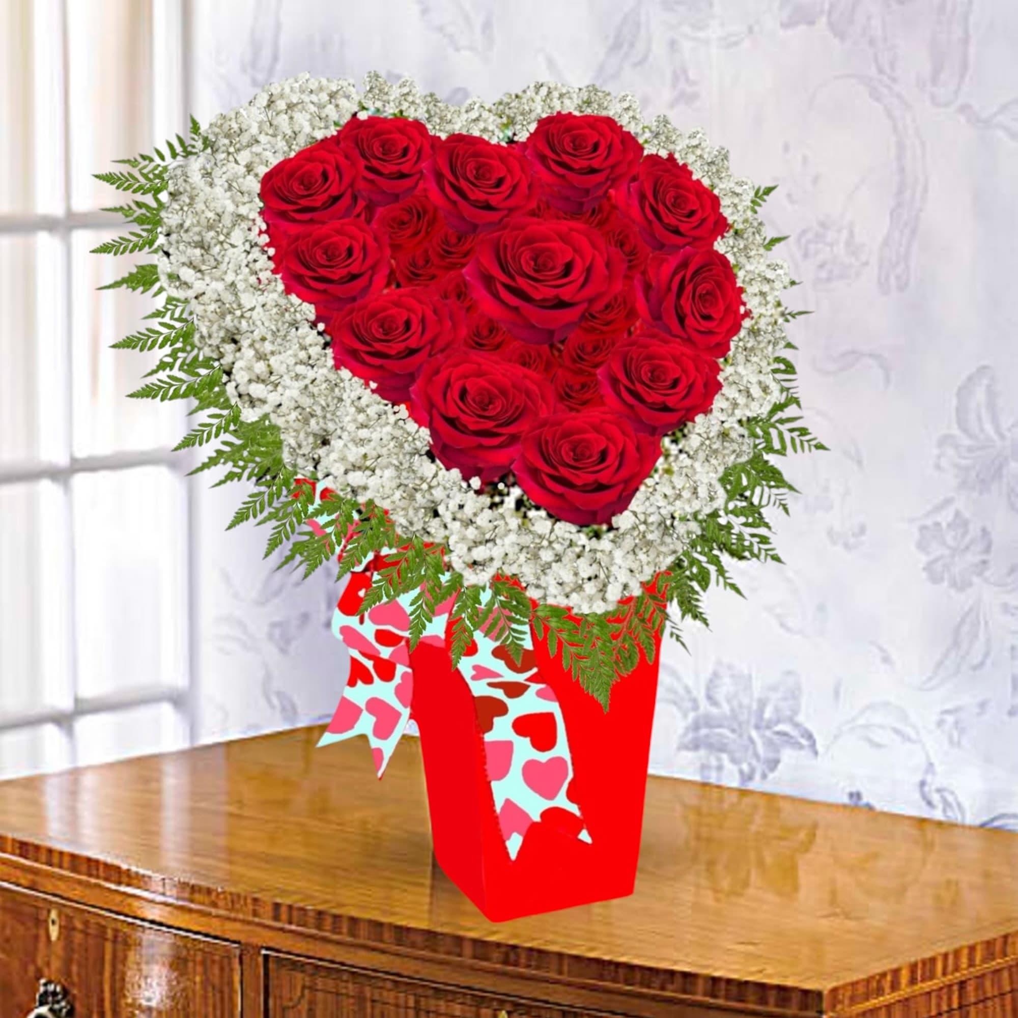 Heart-shaped red rose arrangement with white filler flowers in a red vase