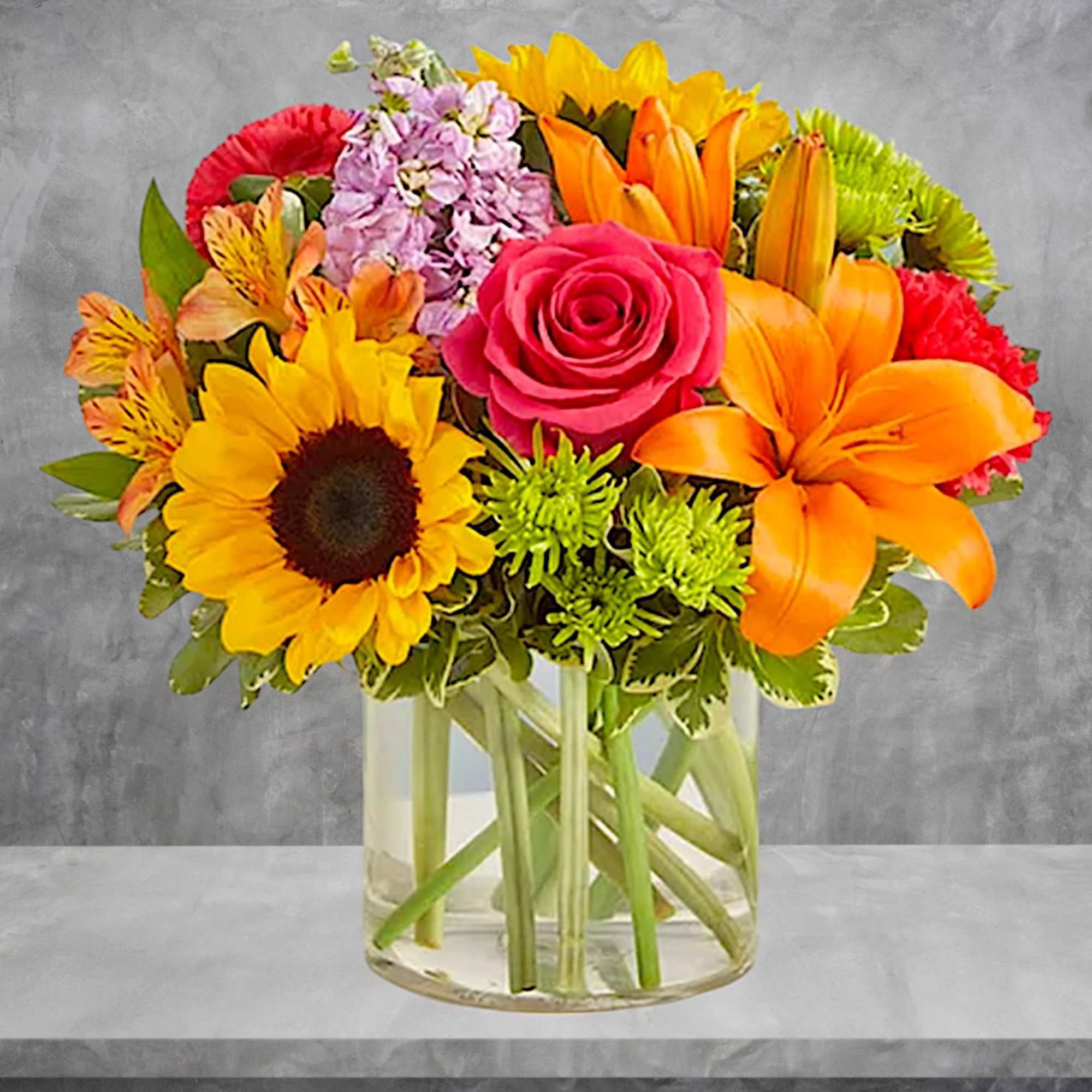 Colorful mixed bouquet in a clear glass vase with a pink rose and sunflowers
