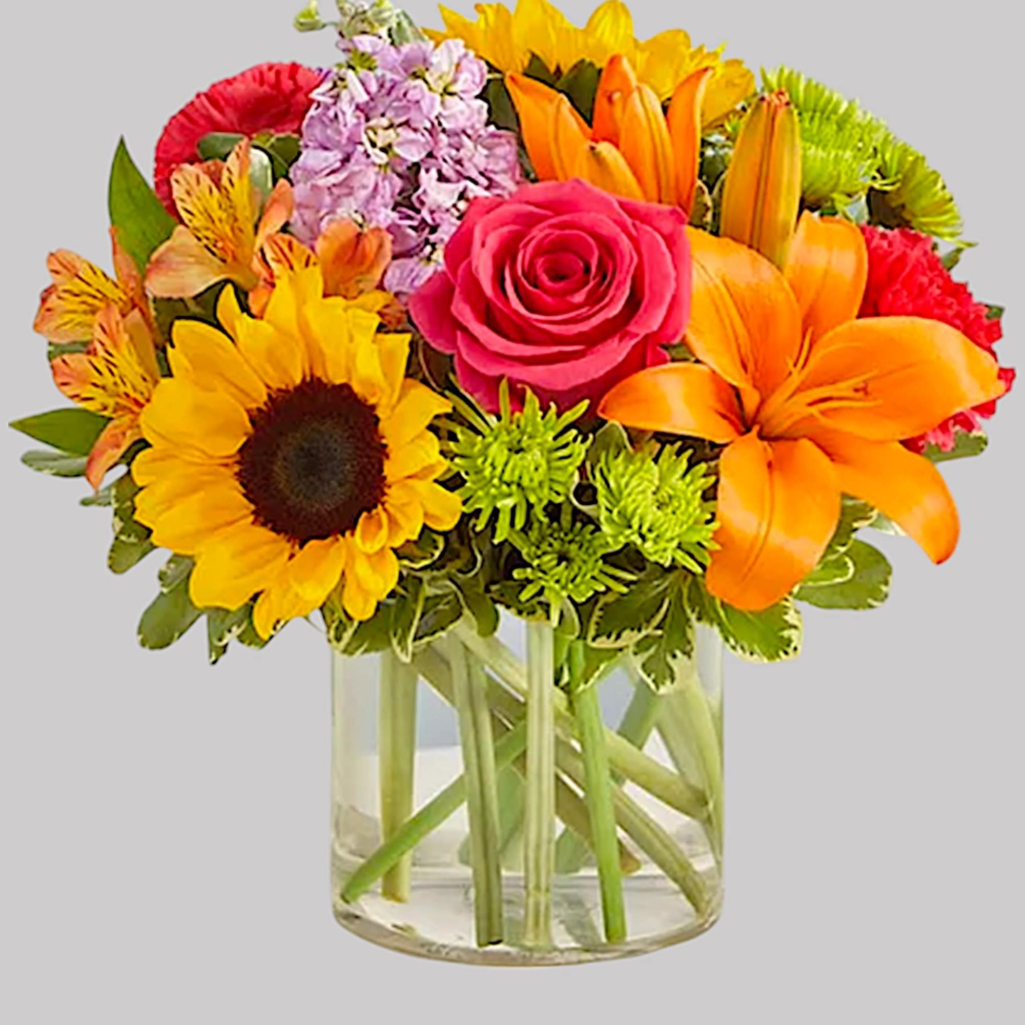 Bright mixed bouquet in a clear glass vase with sunflower, rose, lily, and chrysanthemum blooms