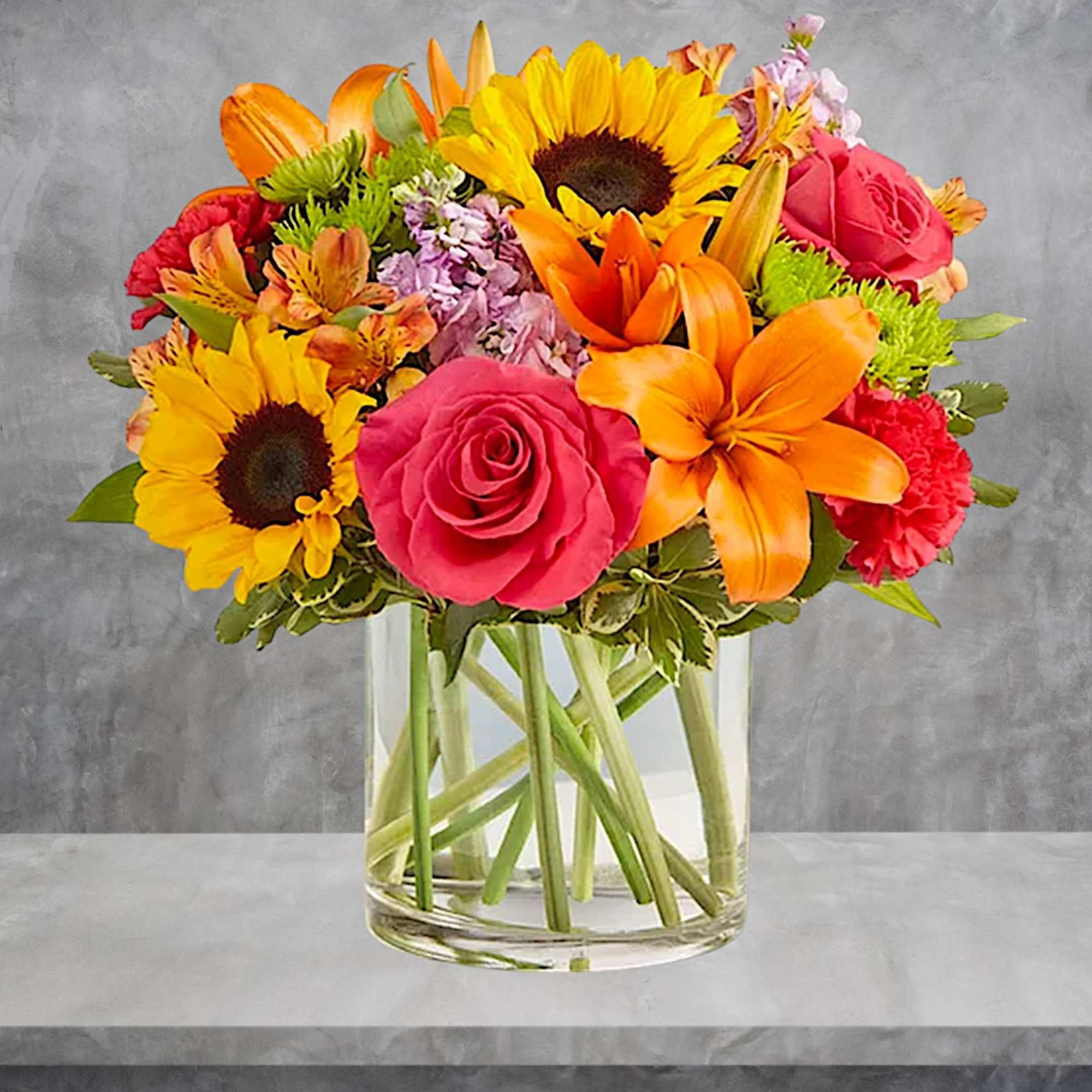 Mixed bouquet of sunflowers, roses, lilies, and carnations in a glass vase