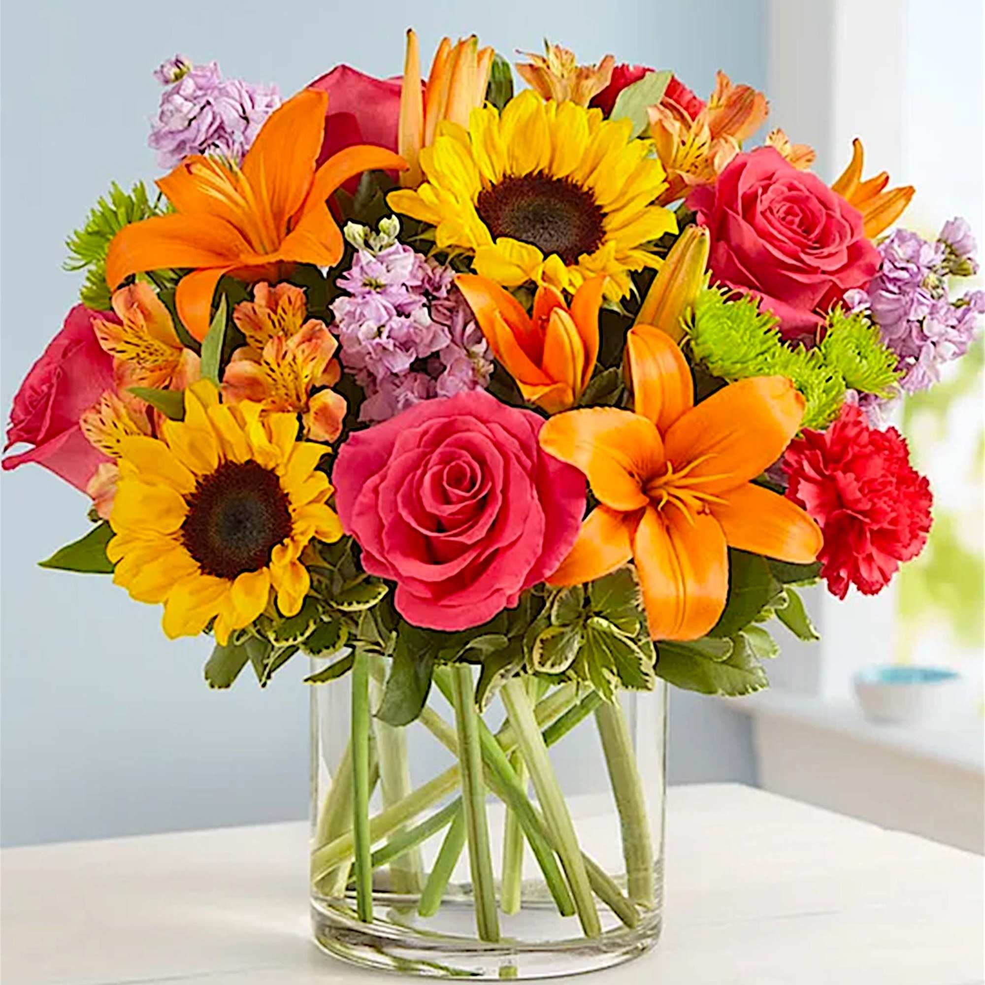 Bright mixed bouquet of sunflowers, roses, and lilies in a glass vase