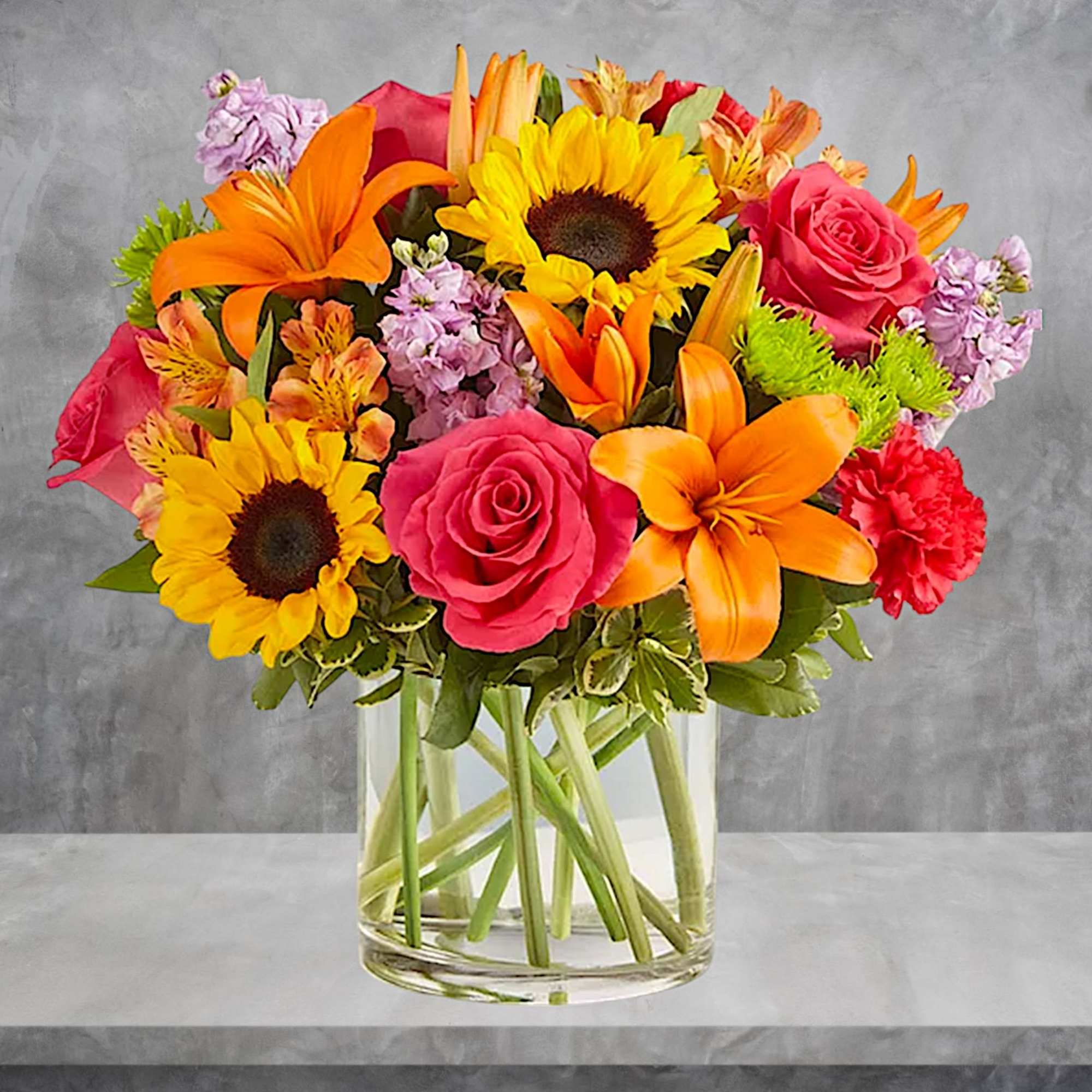 Bright mixed bouquet of sunflowers, roses, lilies, and carnations in a glass vase