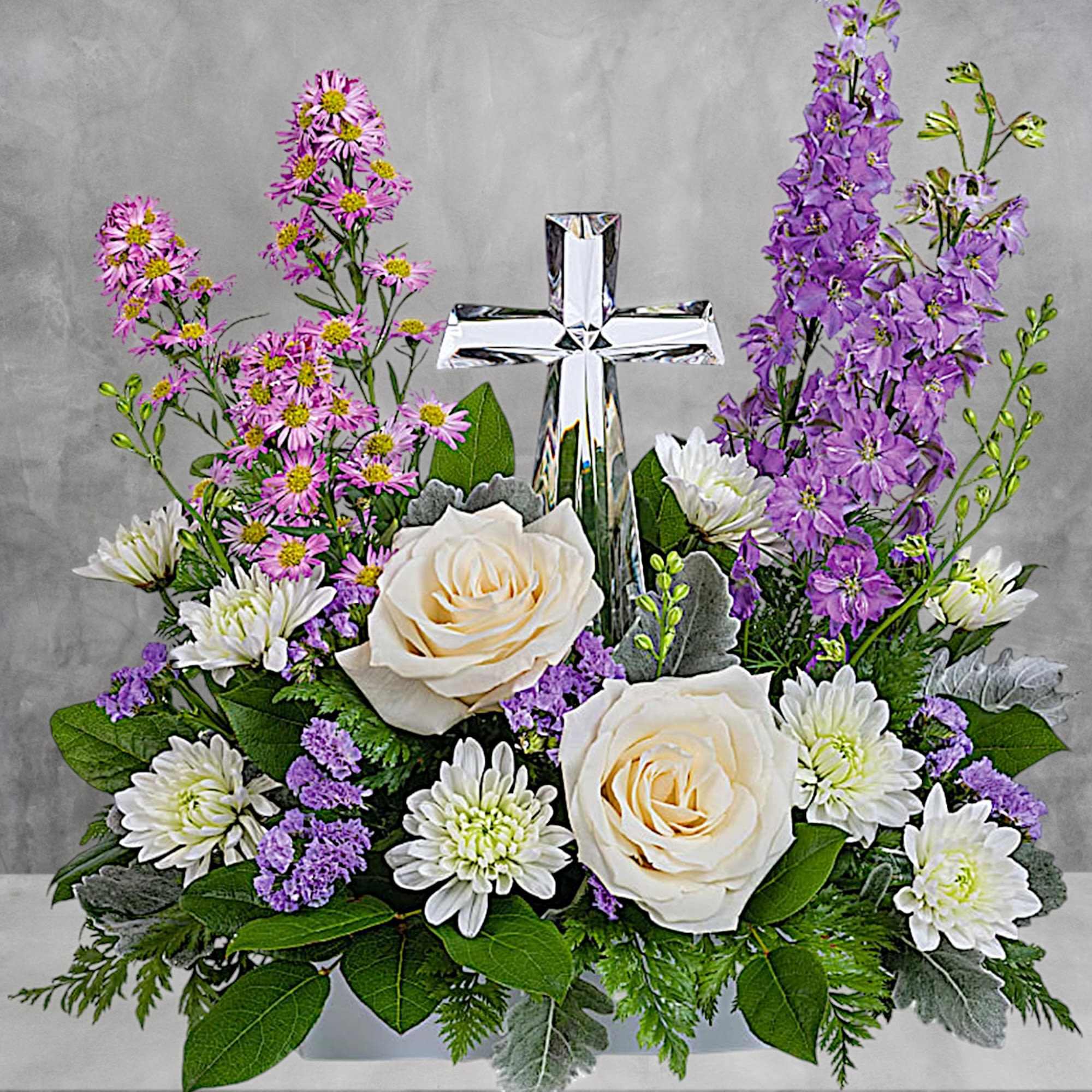 White roses and purple flowers arranged around a silver cross