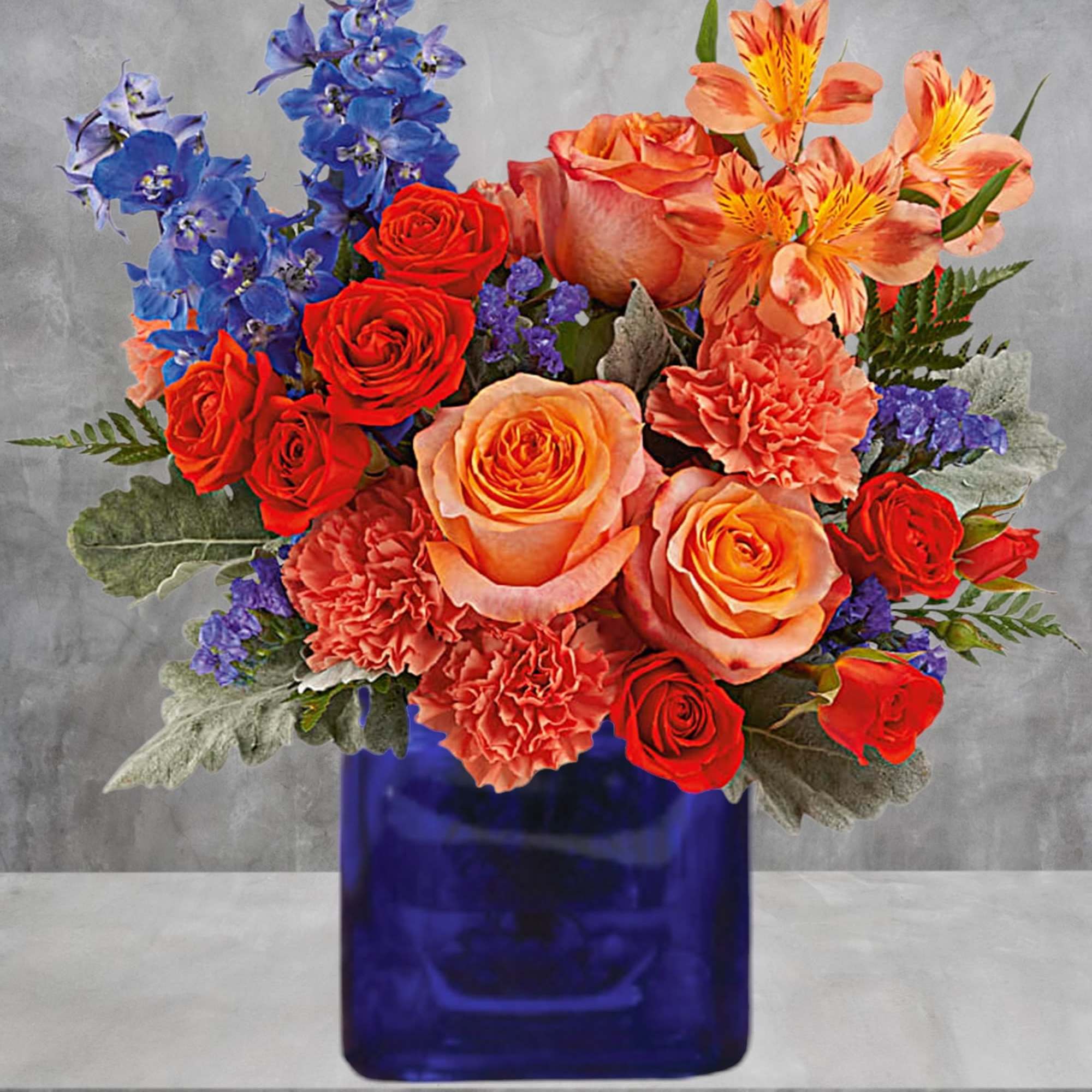 Mixed bouquet of roses, carnations, and blue flowers in a cobalt vase