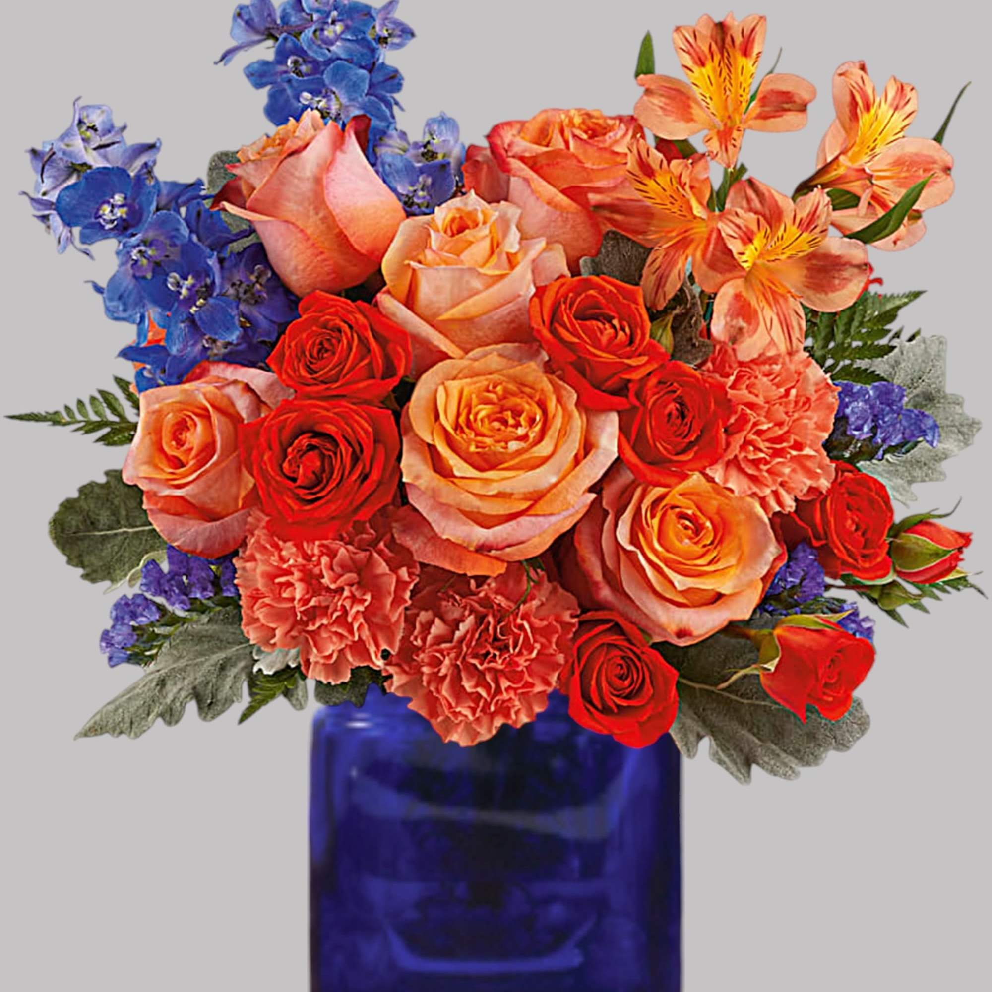 Mixed bouquet of roses, carnations, and blue flowers in a cobalt vase
