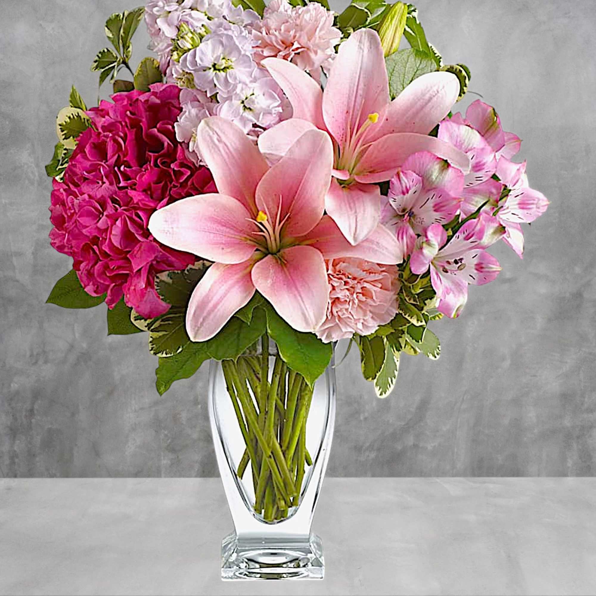 Pink lilies and mixed pink flowers arranged in a clear glass vase