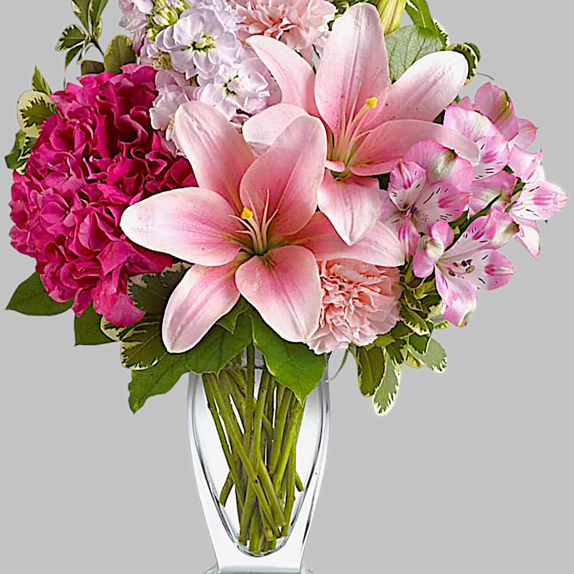 Pink lilies and mixed blooms in a clear glass vase