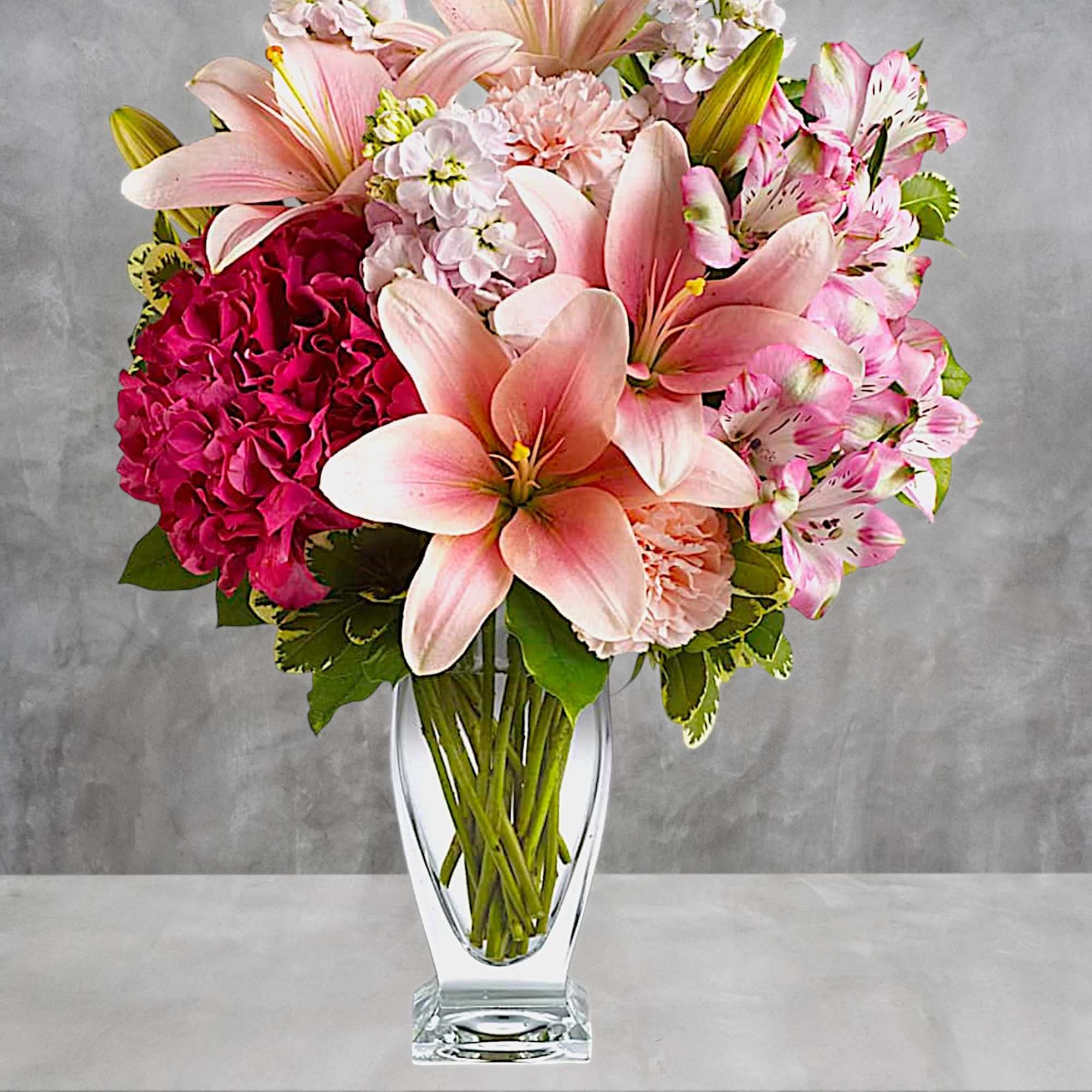 Pink lilies and hydrangeas arranged in a clear glass vase, photo 2 of 4