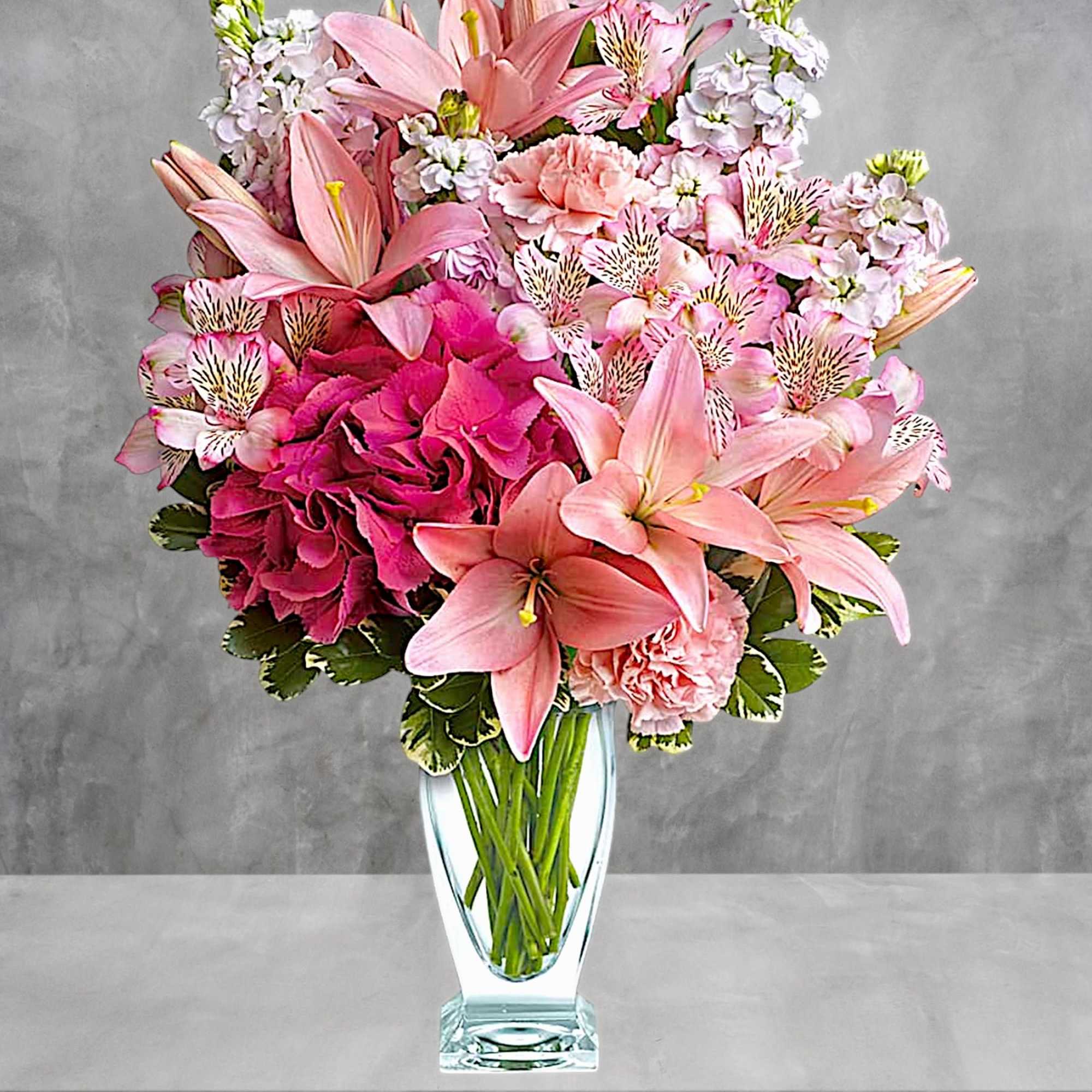 Pink lilies and mixed pink flowers arranged in a clear glass vase