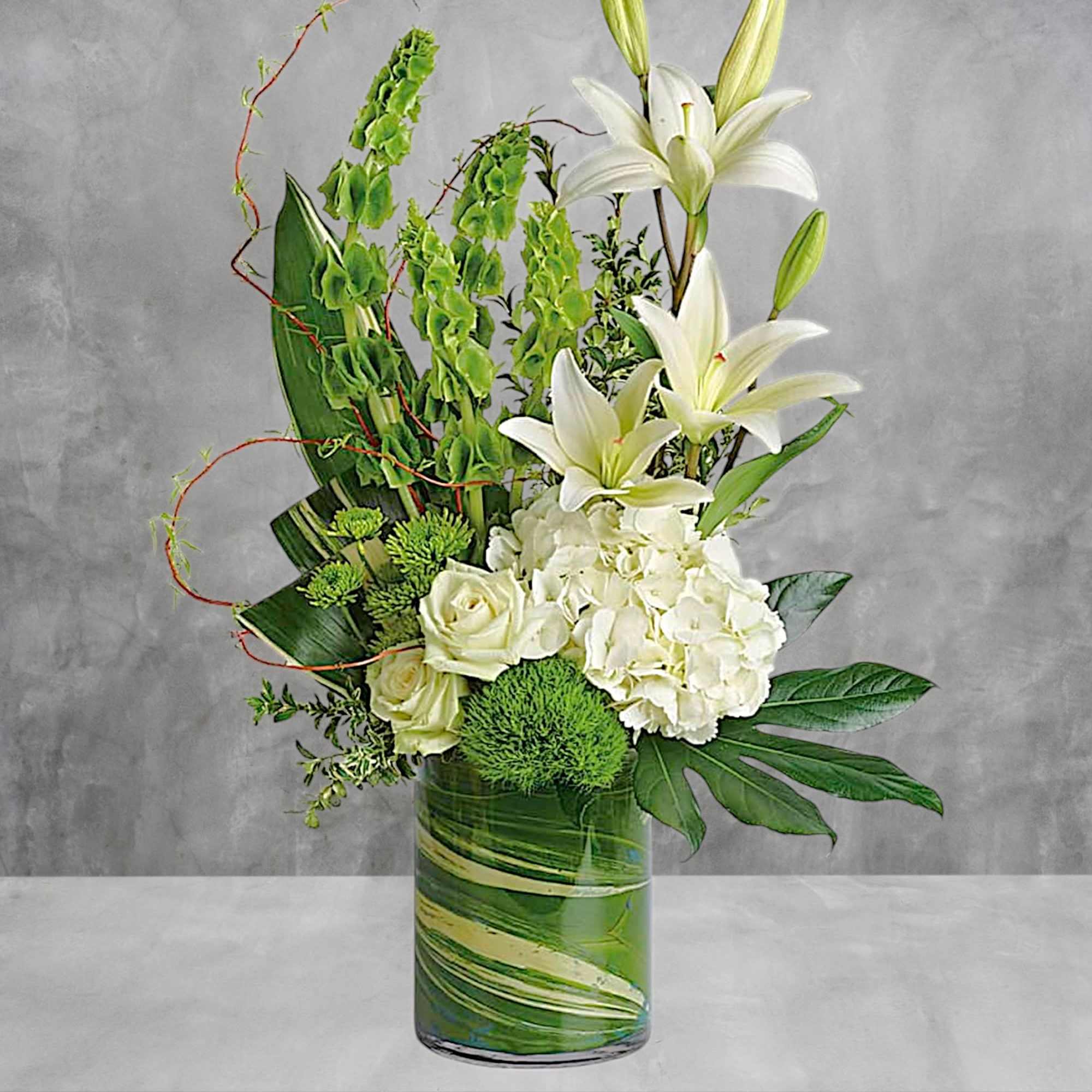 White lilies and roses arranged in a glass vase with green accents