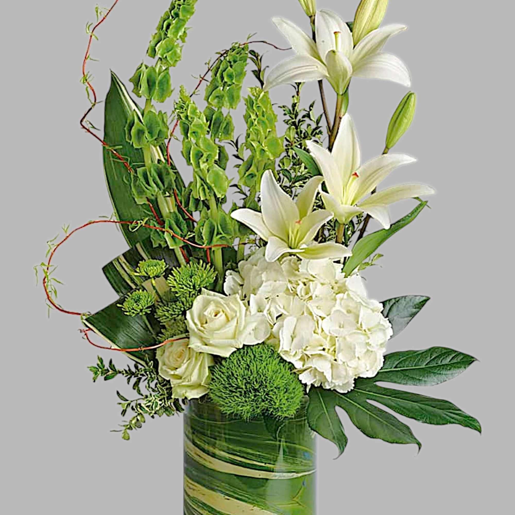 White lilies and roses arranged with green accents in a glass vase