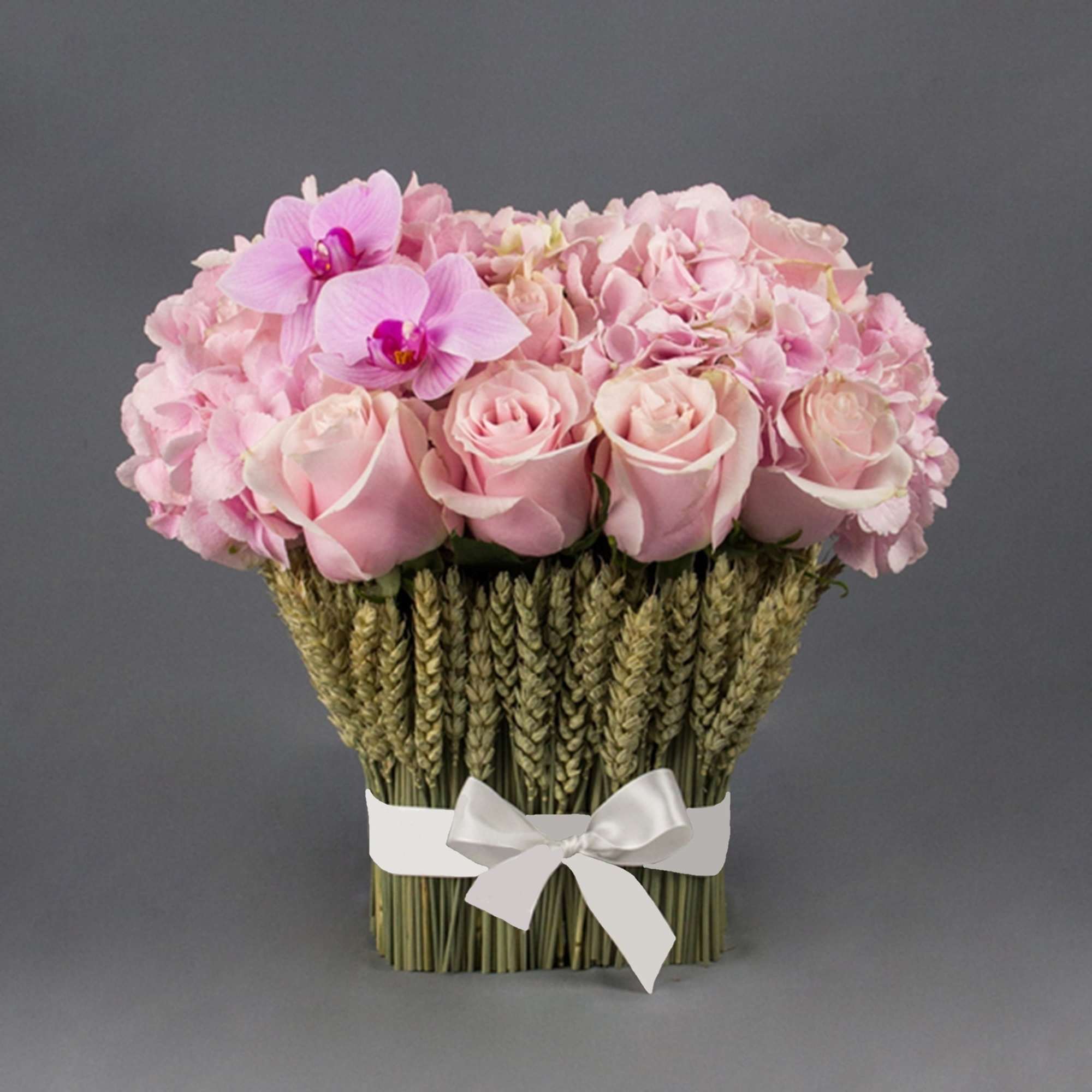 Pink roses and orchids arranged in a wheat-wrapped bouquet with a white ribbon