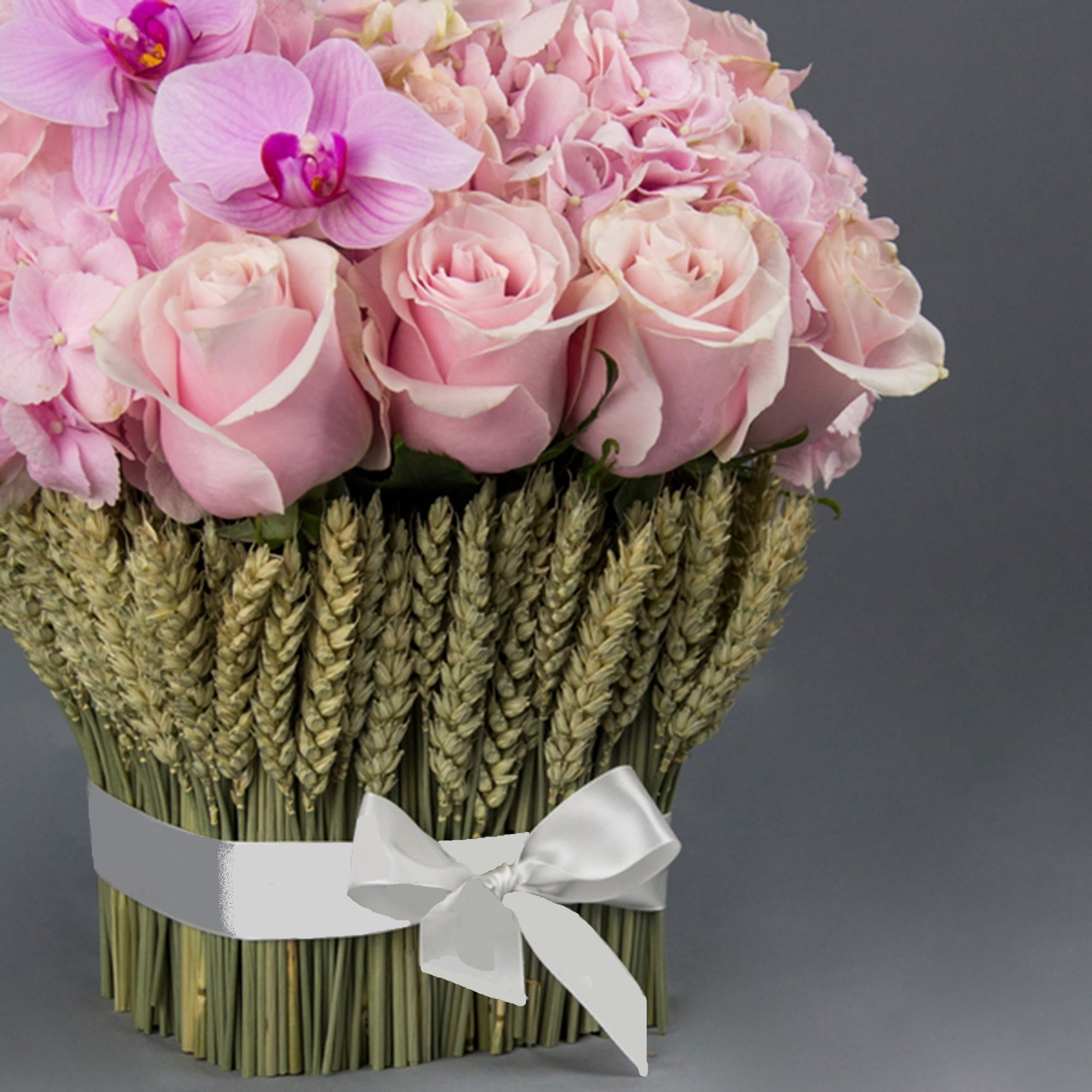 Pink roses and orchids arranged above bundled wheat with a white ribbon