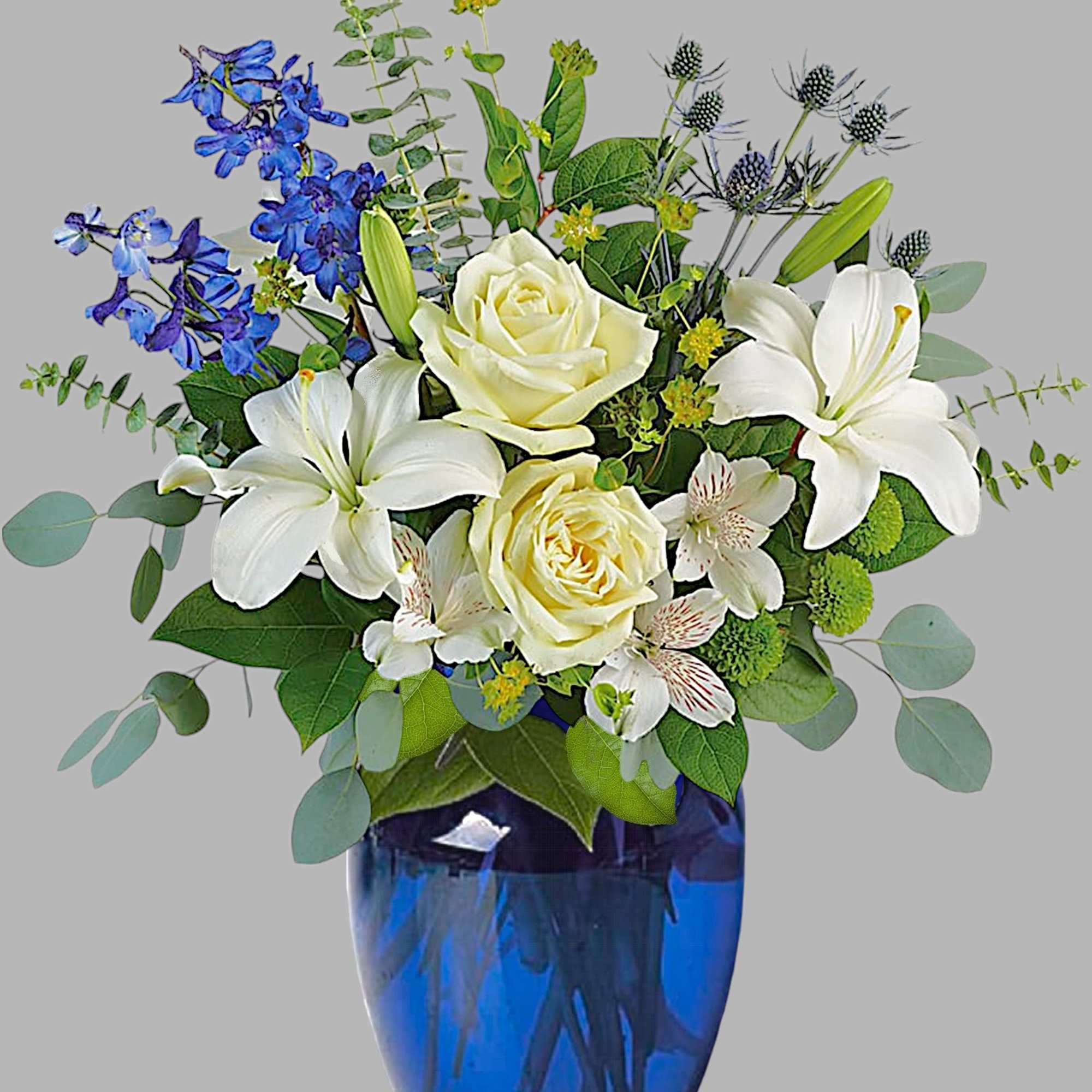 White lilies and roses in a blue glass vase with blue flowers