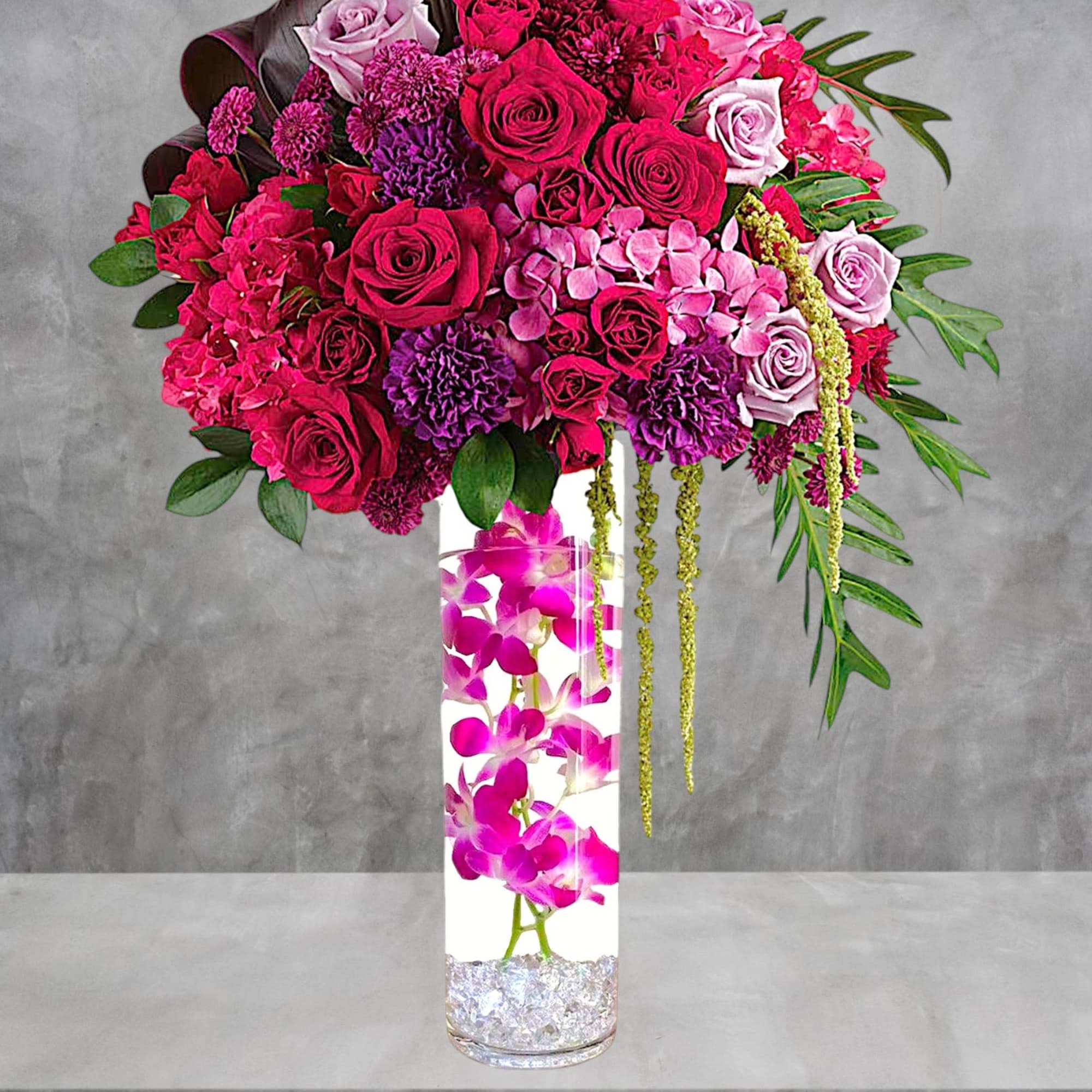 Pink and purple rose arrangement in a tall glass vase with orchids