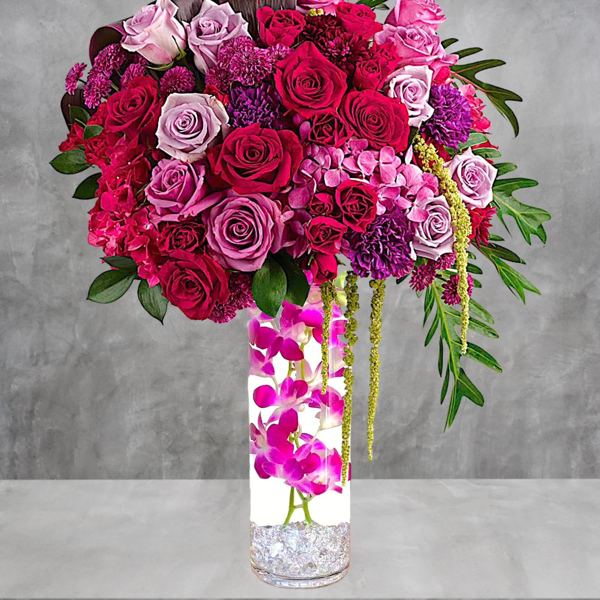 Tall bouquet of pink and red roses in a clear vase with orchids