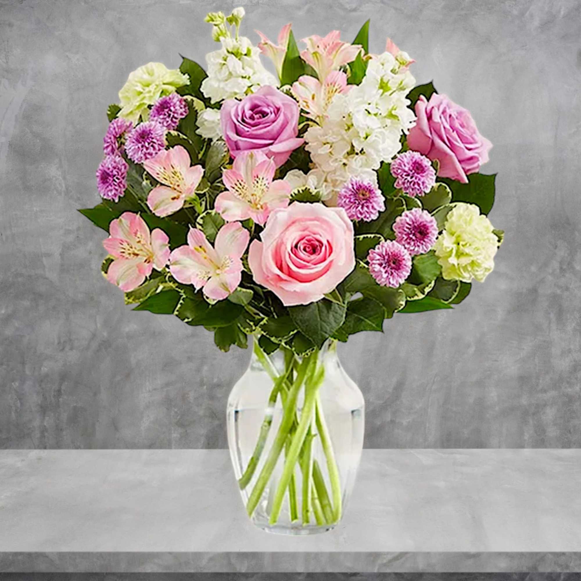 Pink roses and mixed pastel flowers arranged in a clear glass vase
