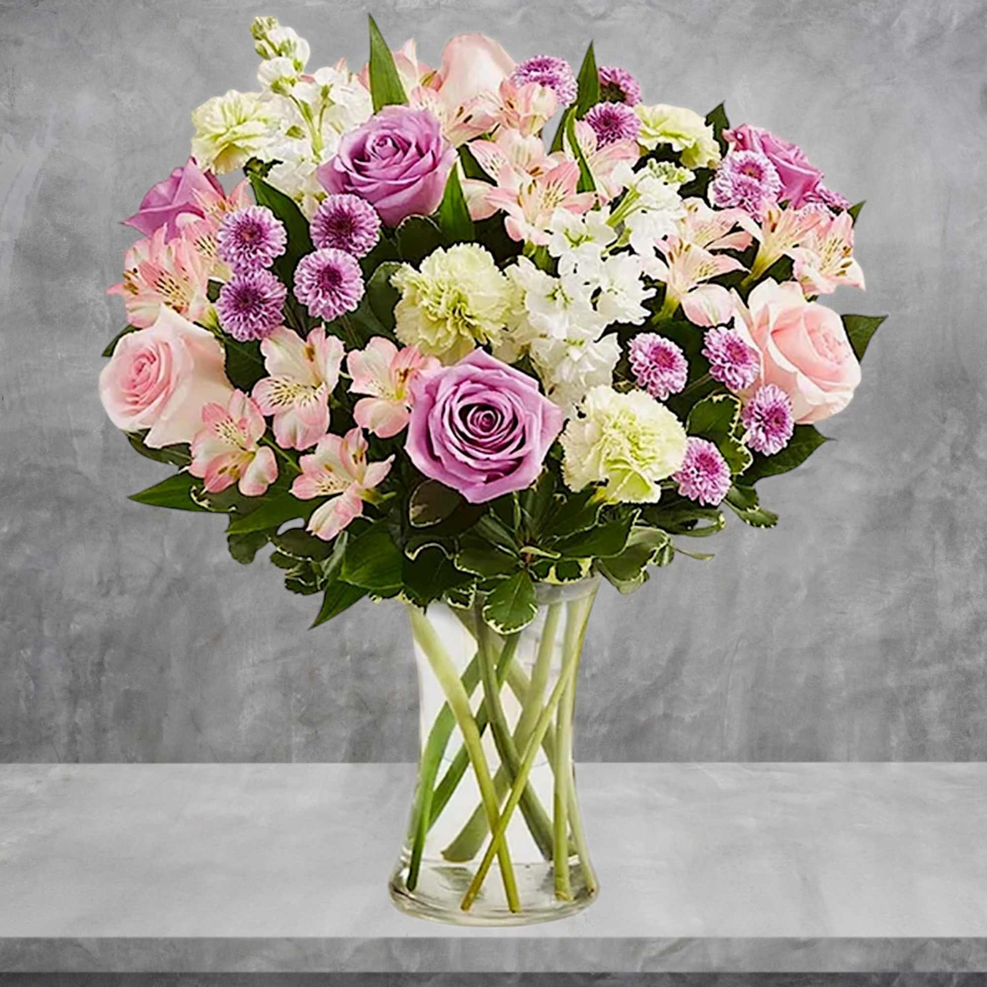 Pink and lavender roses with mixed blooms in a clear glass vase