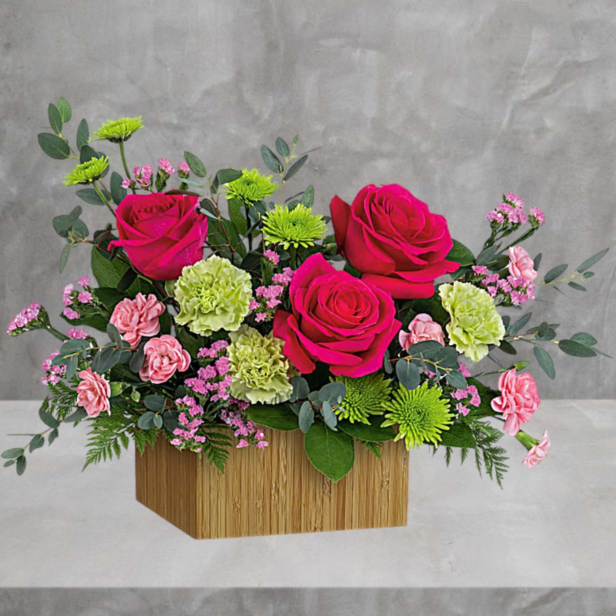 Pink roses and carnations in a wooden box with green filler flowers