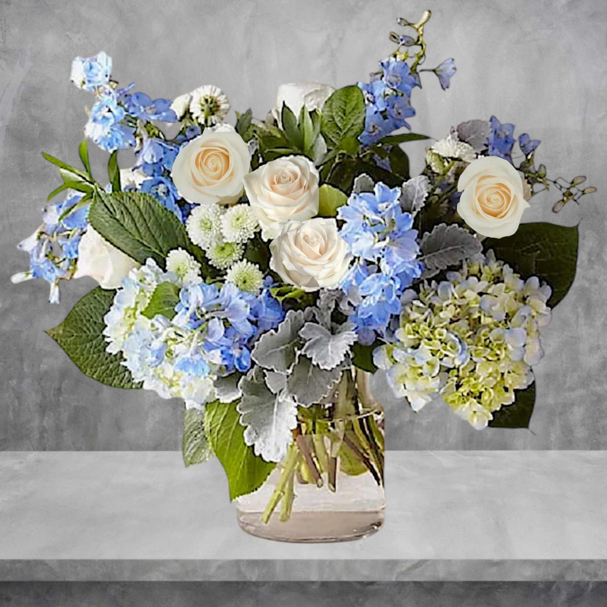 Bouquet of white roses and blue flowers in a clear glass vase