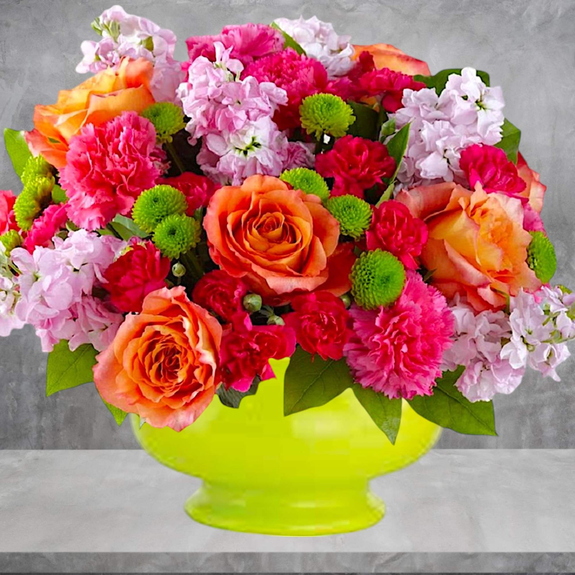 Bright mixed bouquet of roses, carnations, and green button mums in a lime vase