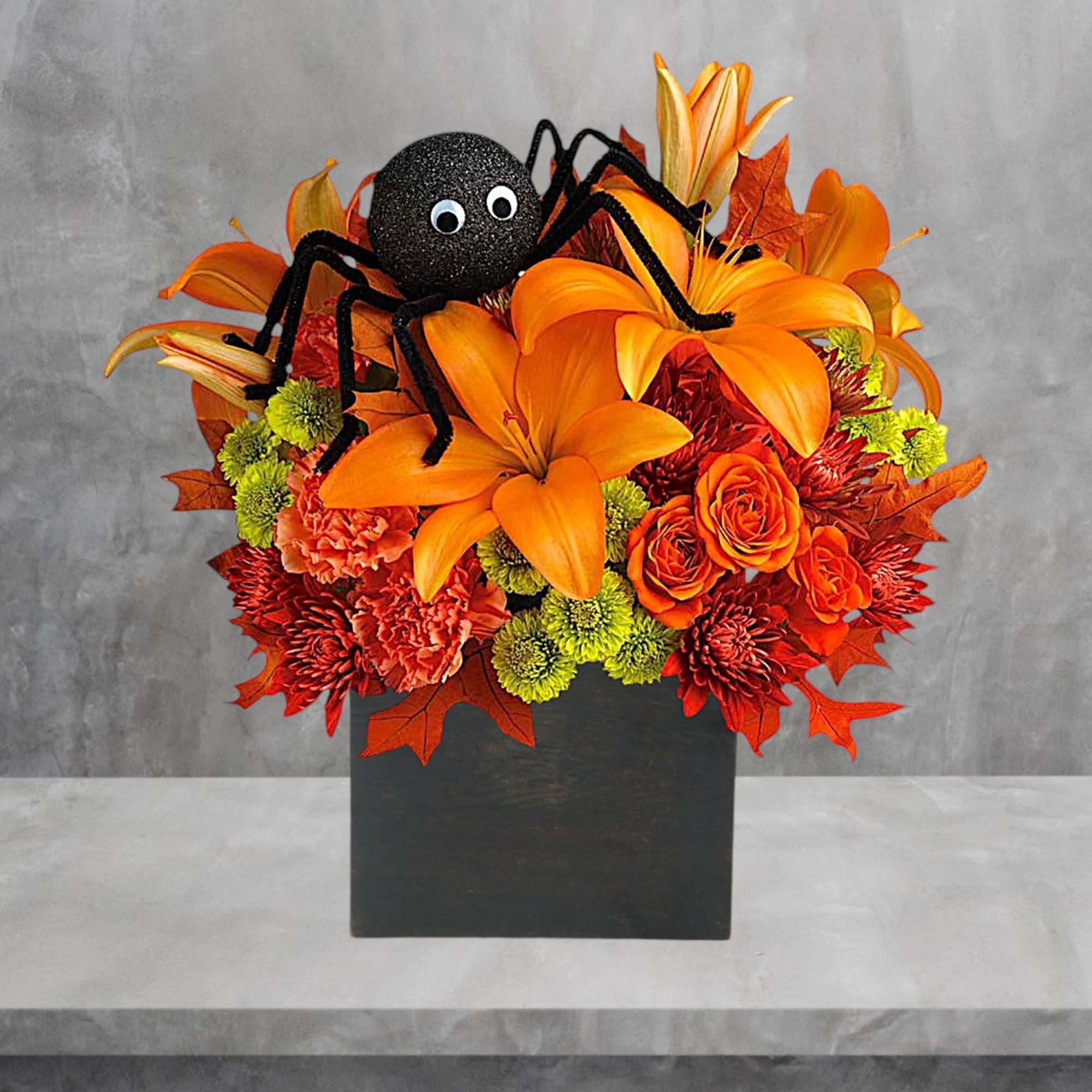 Orange floral arrangement with a decorative spider and black container