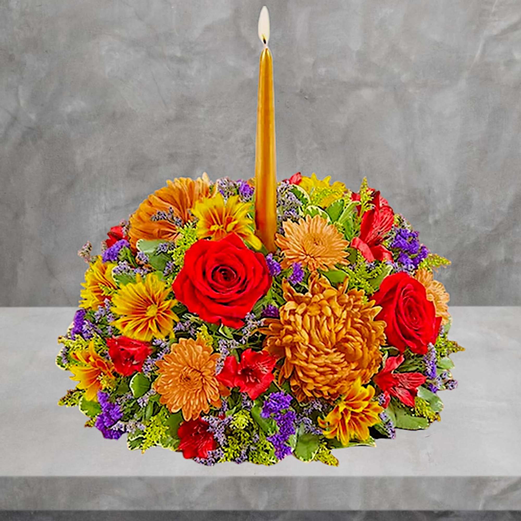 Round floral arrangement with a tall gold taper candle in the center