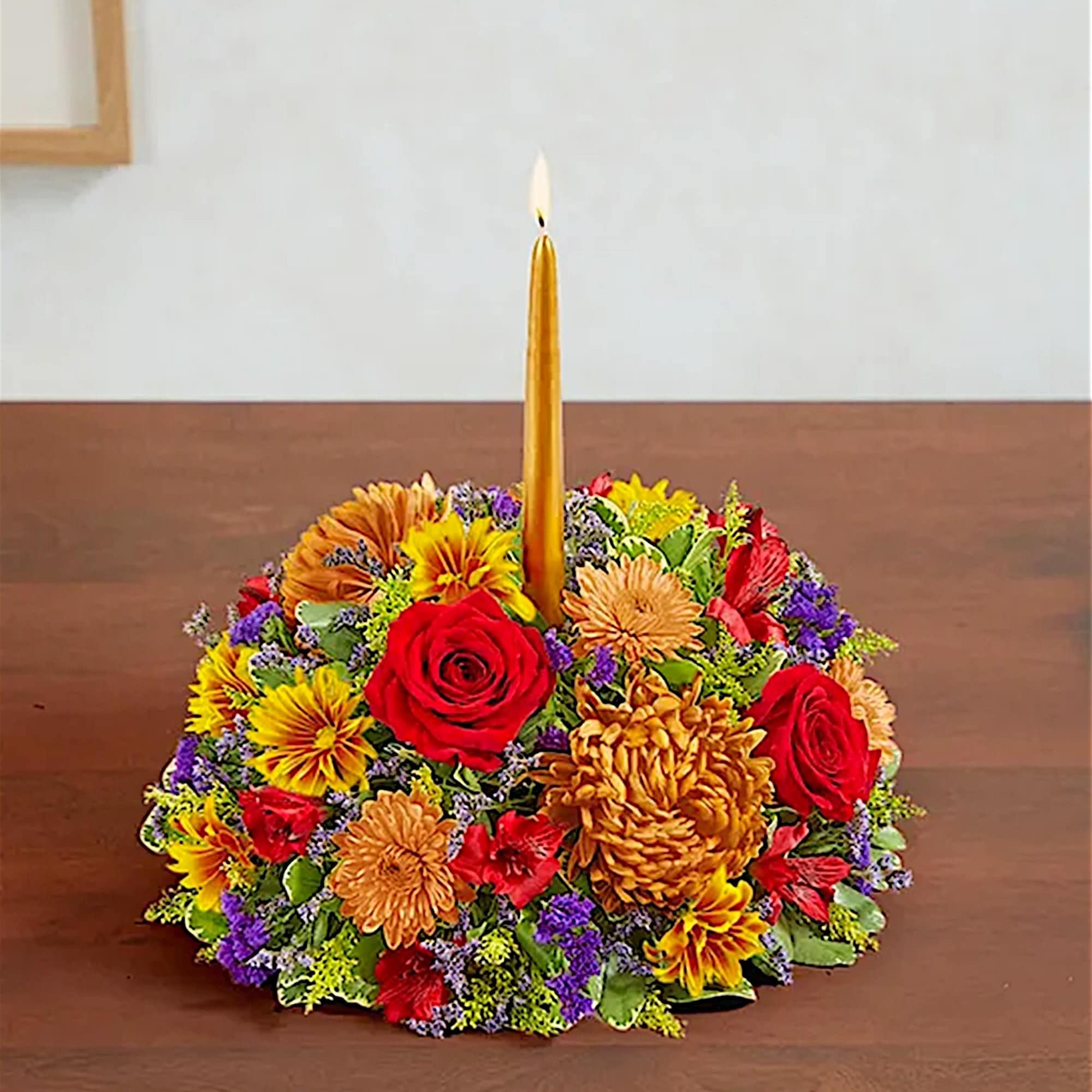 Round floral centerpiece with a lit gold candle in the middle