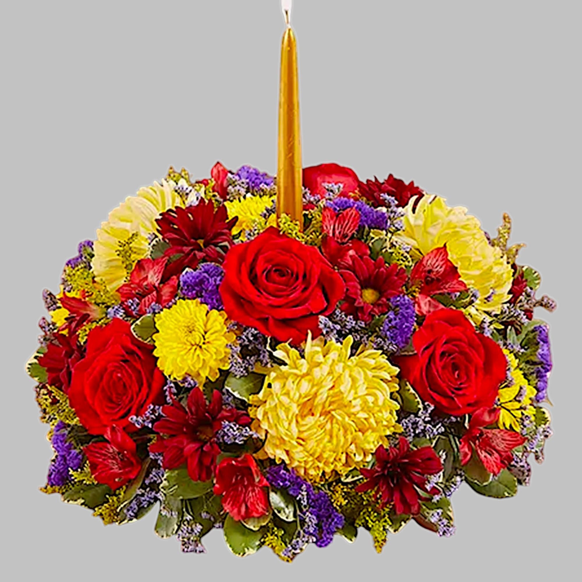 Round floral arrangement with red roses, yellow and purple blooms, and a tall gold candle