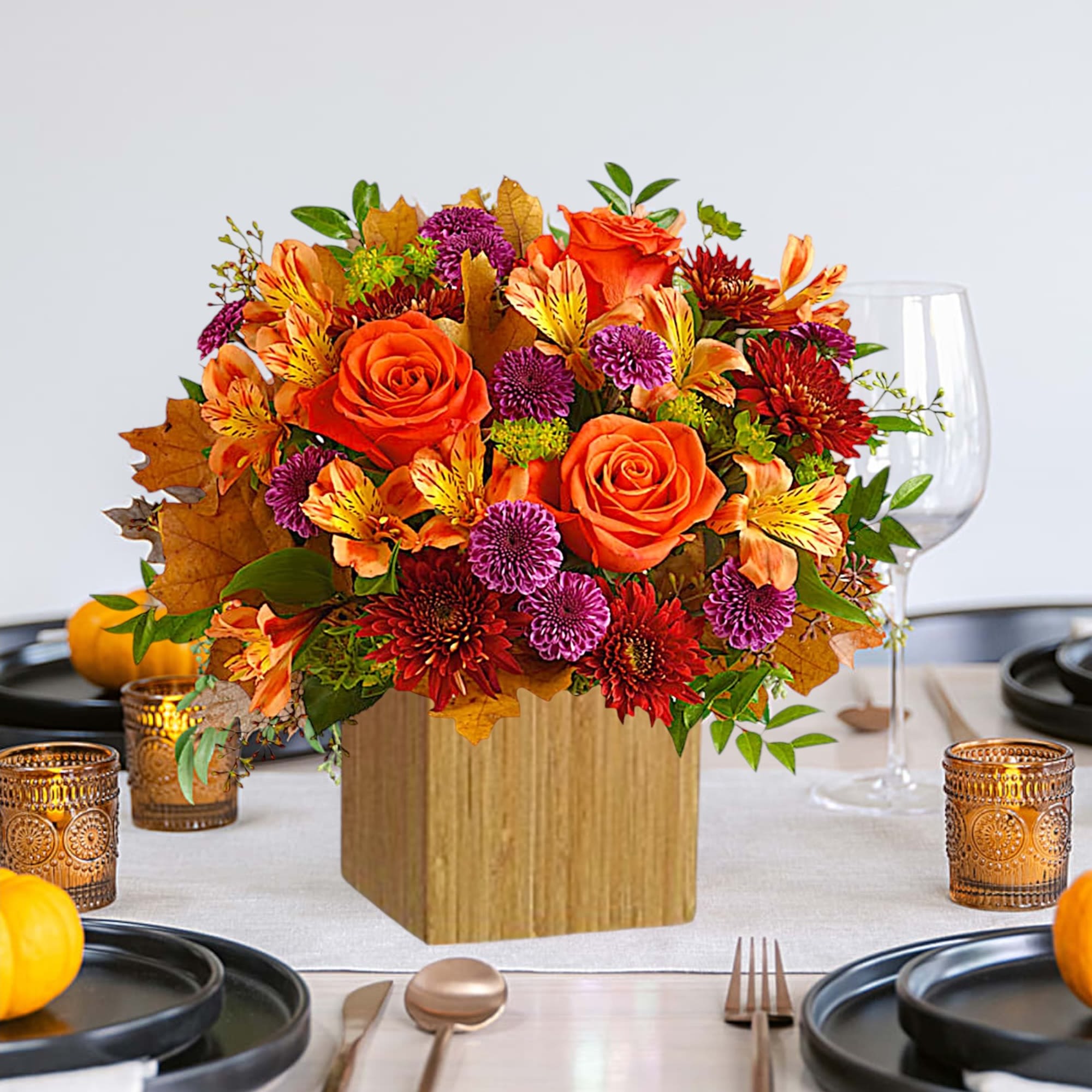 Autumn floral centerpiece with orange roses and purple mums in a wooden cube vase