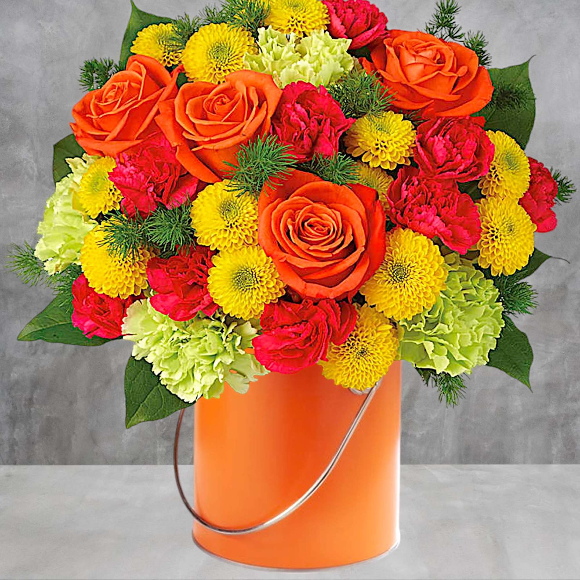 Orange roses, yellow mums, and pink carnations in an orange bucket
