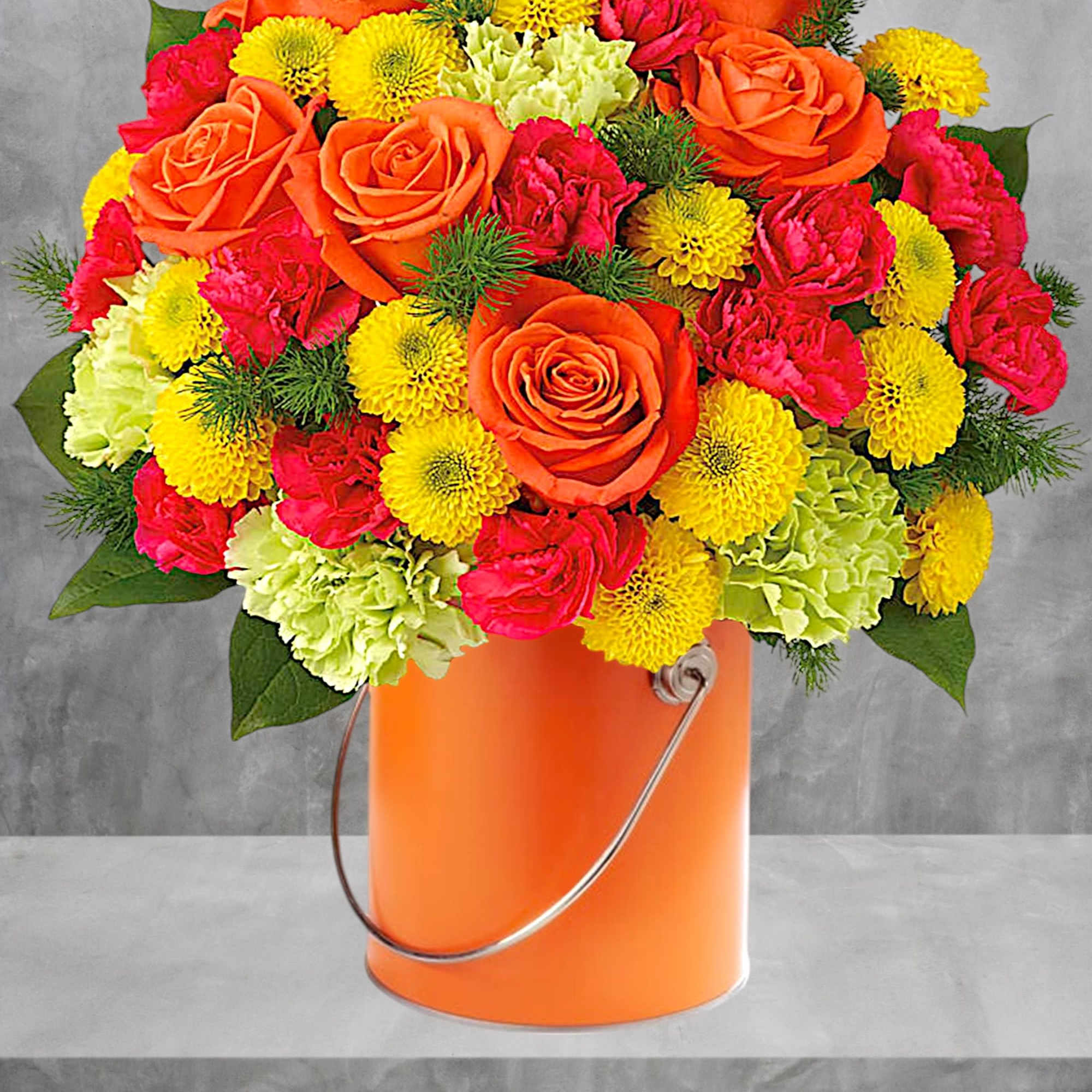 Orange roses, pink carnations, and yellow pompons in an orange bucket