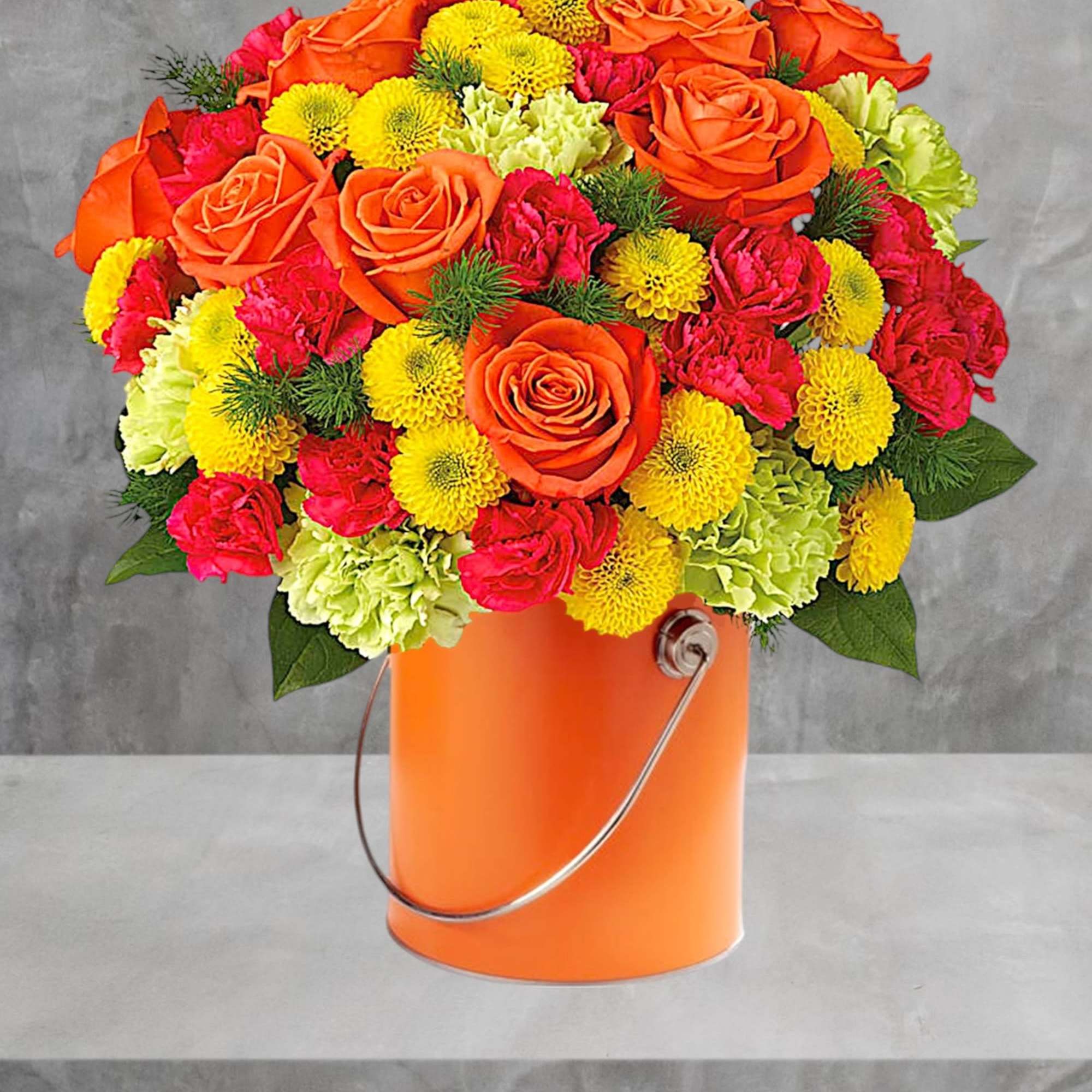 Bouquet of orange roses, pink carnations, and yellow mums in an orange bucket