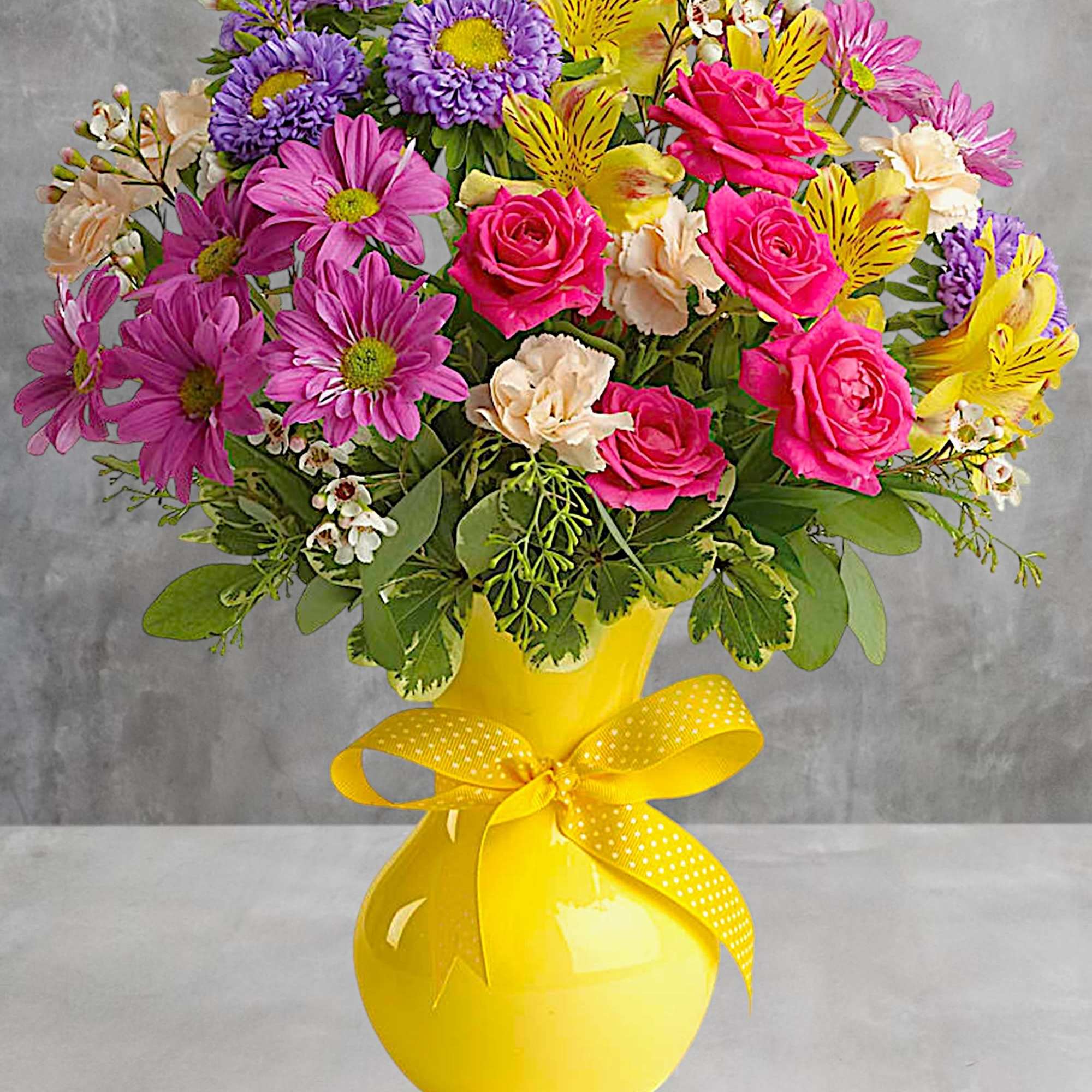 Bouquet of pink, purple, and yellow flowers in a yellow vase with a ribbon