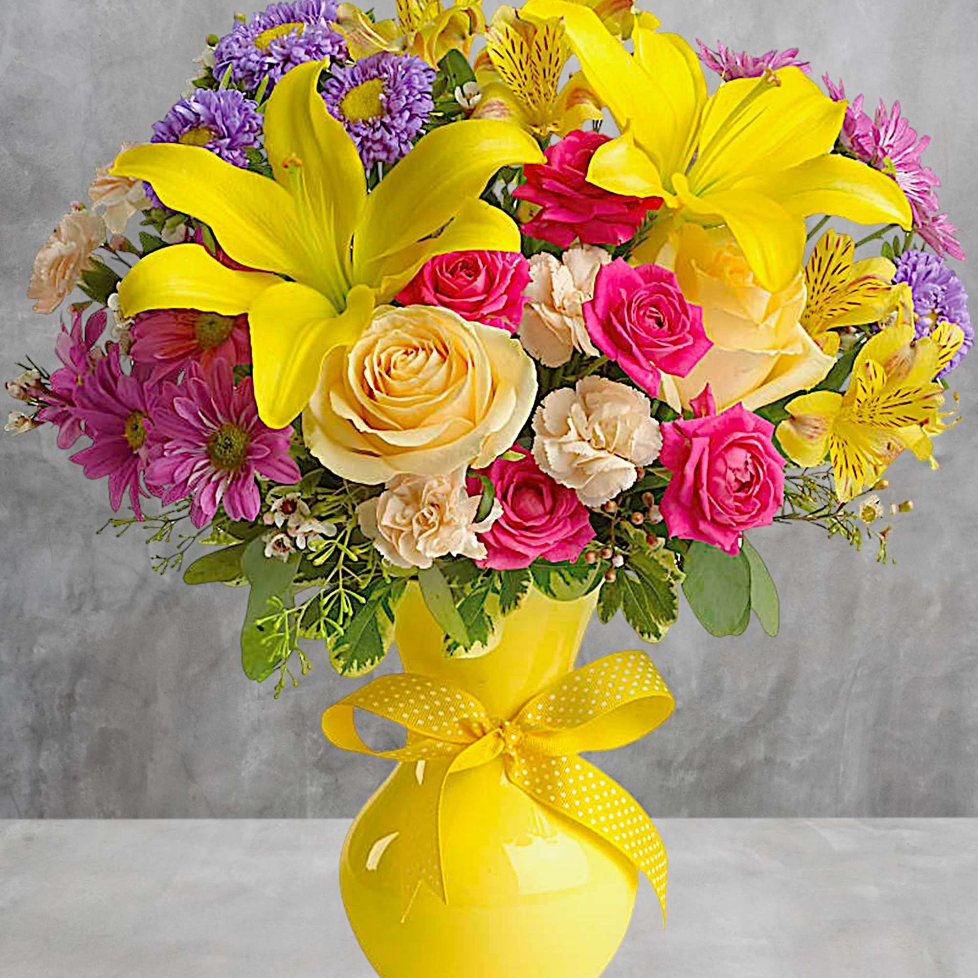 Bright bouquet of yellow lilies, pink roses, and purple daisies in a yellow vase