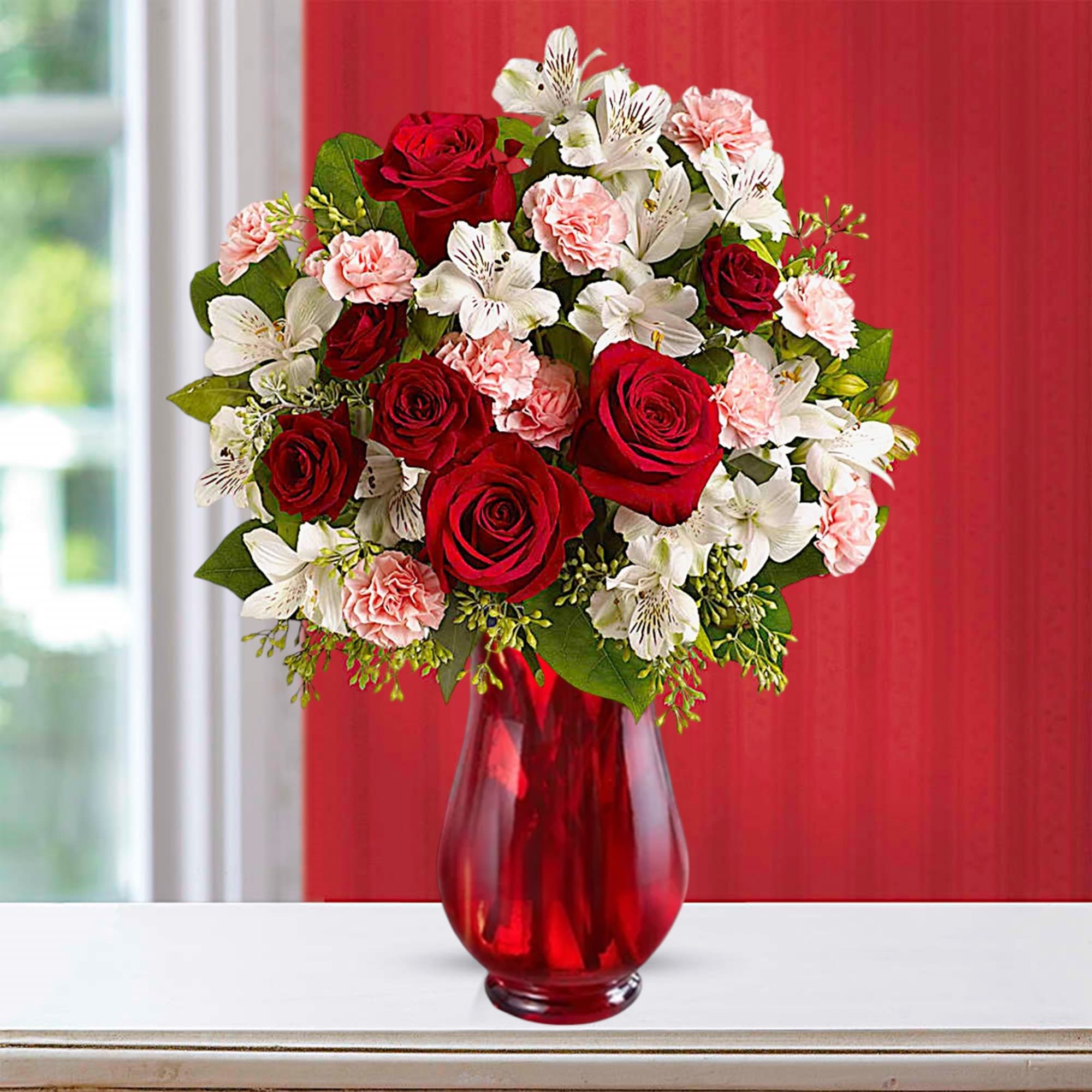 Red roses and white flowers arranged in a red glass vase