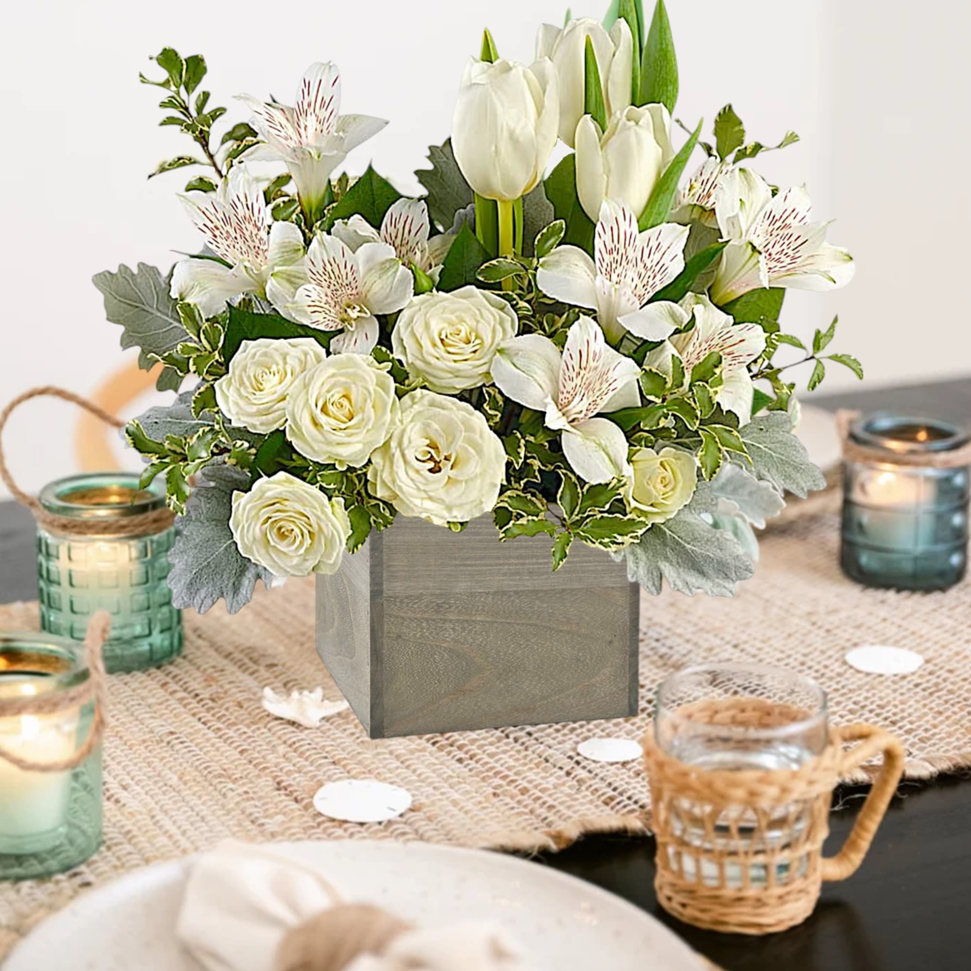 White floral centerpiece in a square vase with candles around it