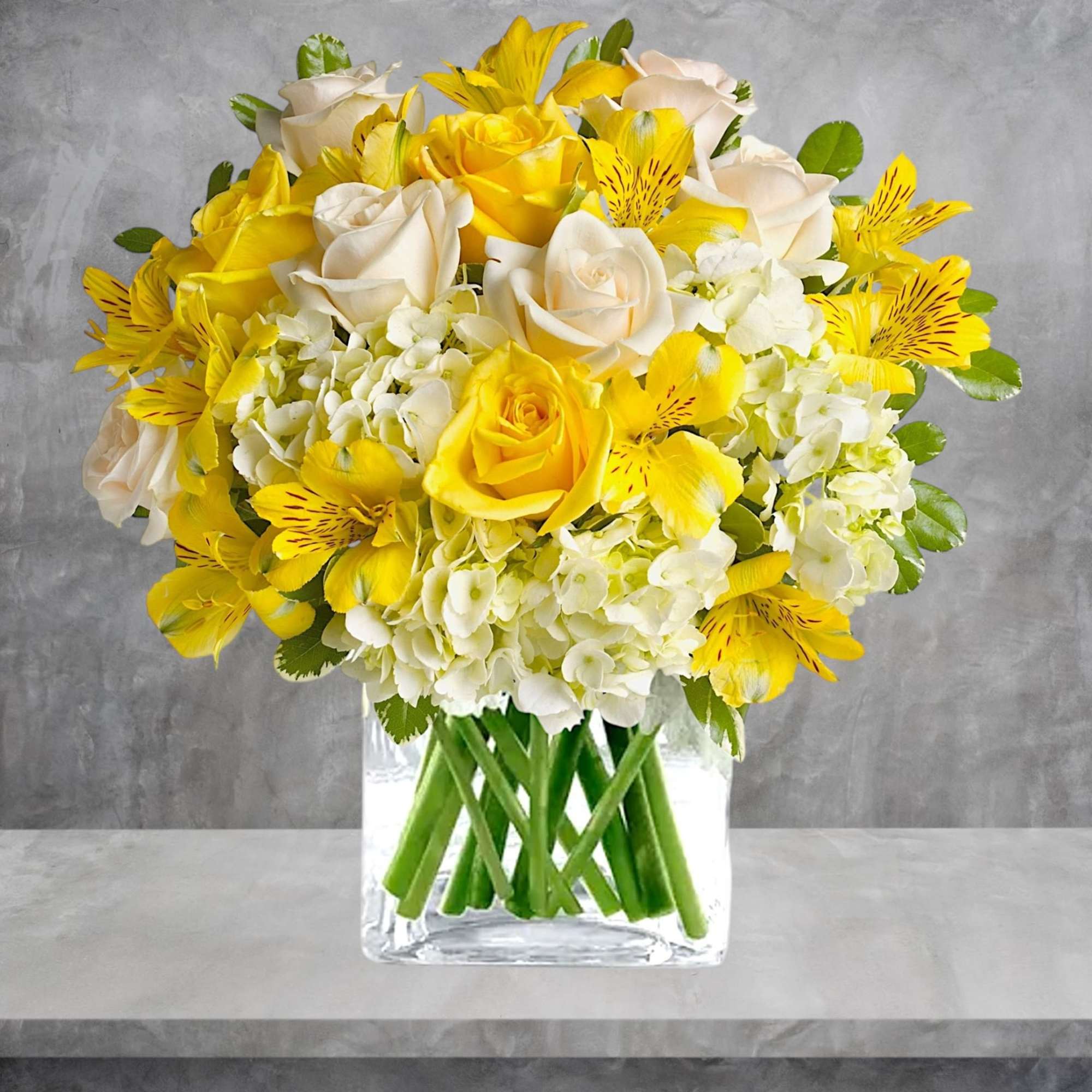 Yellow and white bouquet of roses, hydrangeas, and alstroemeria in a clear vase