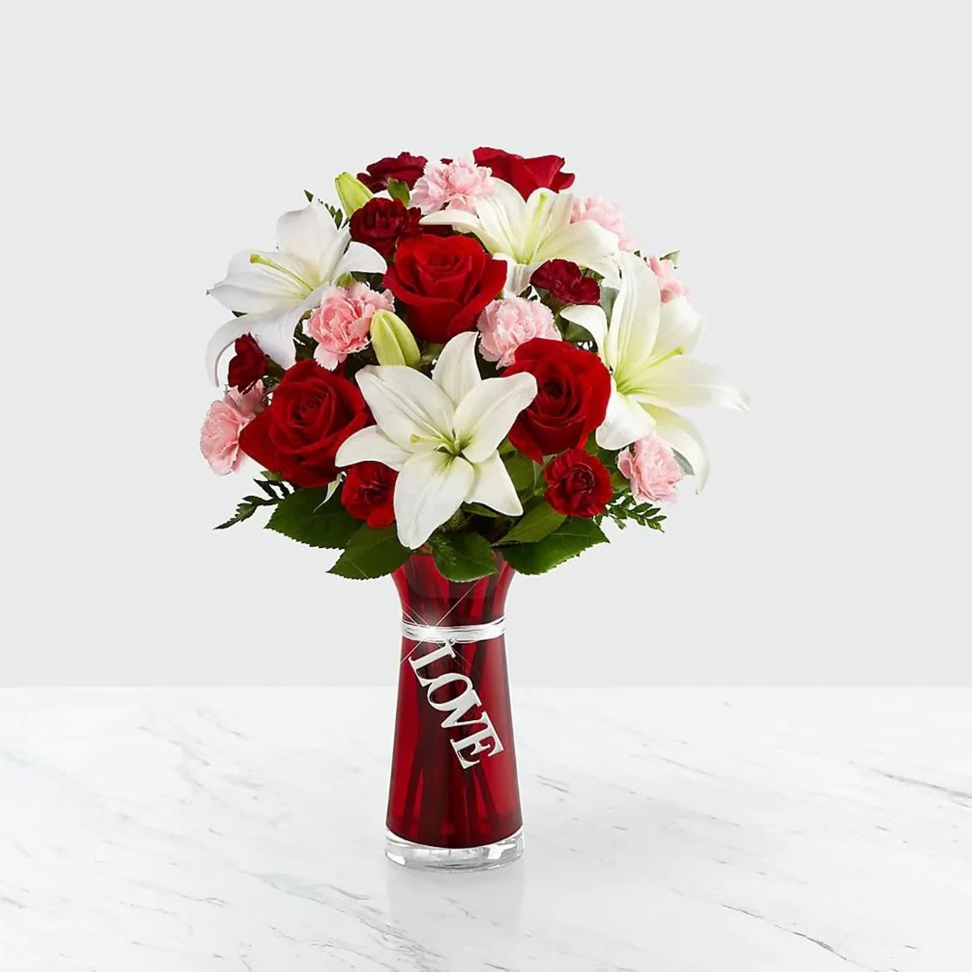 Red roses, white lilies, and pink carnations in a red vase with a LOVE charm