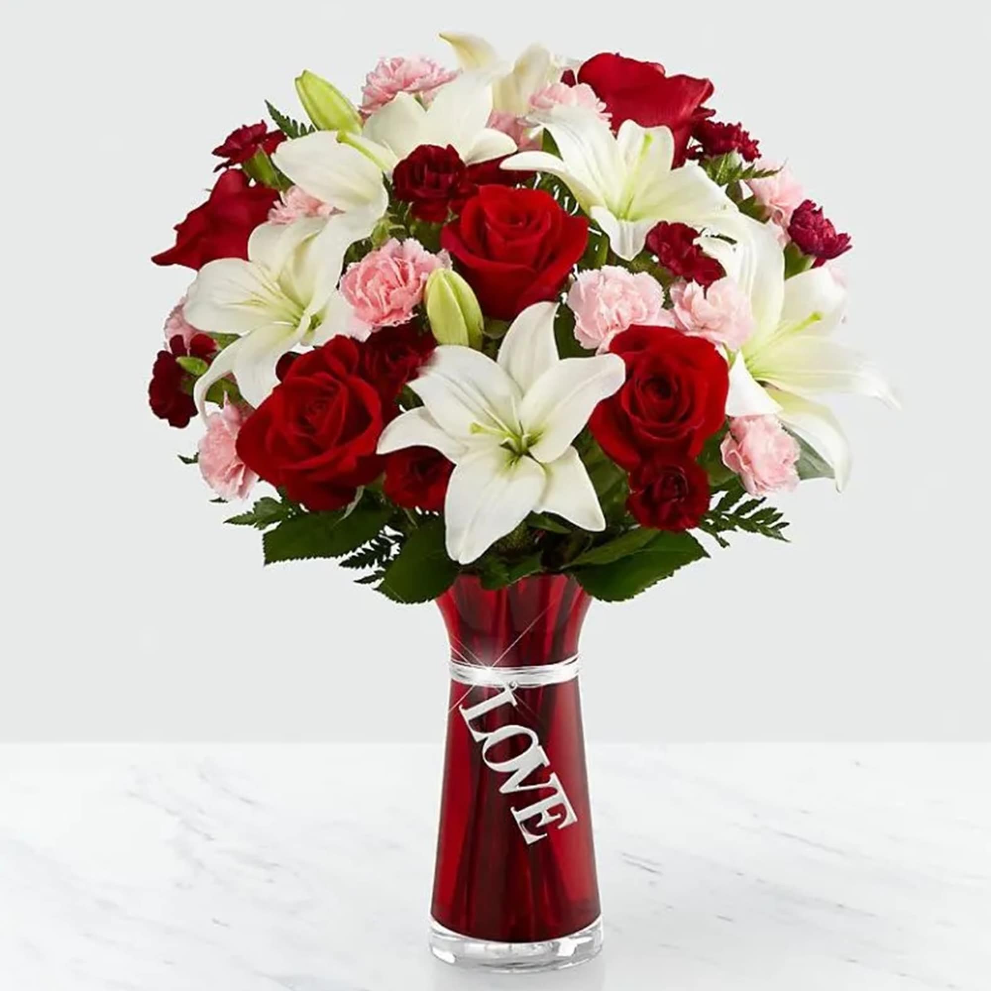 Red roses, white lilies, and pink carnations in a red vase with a LOVE tag