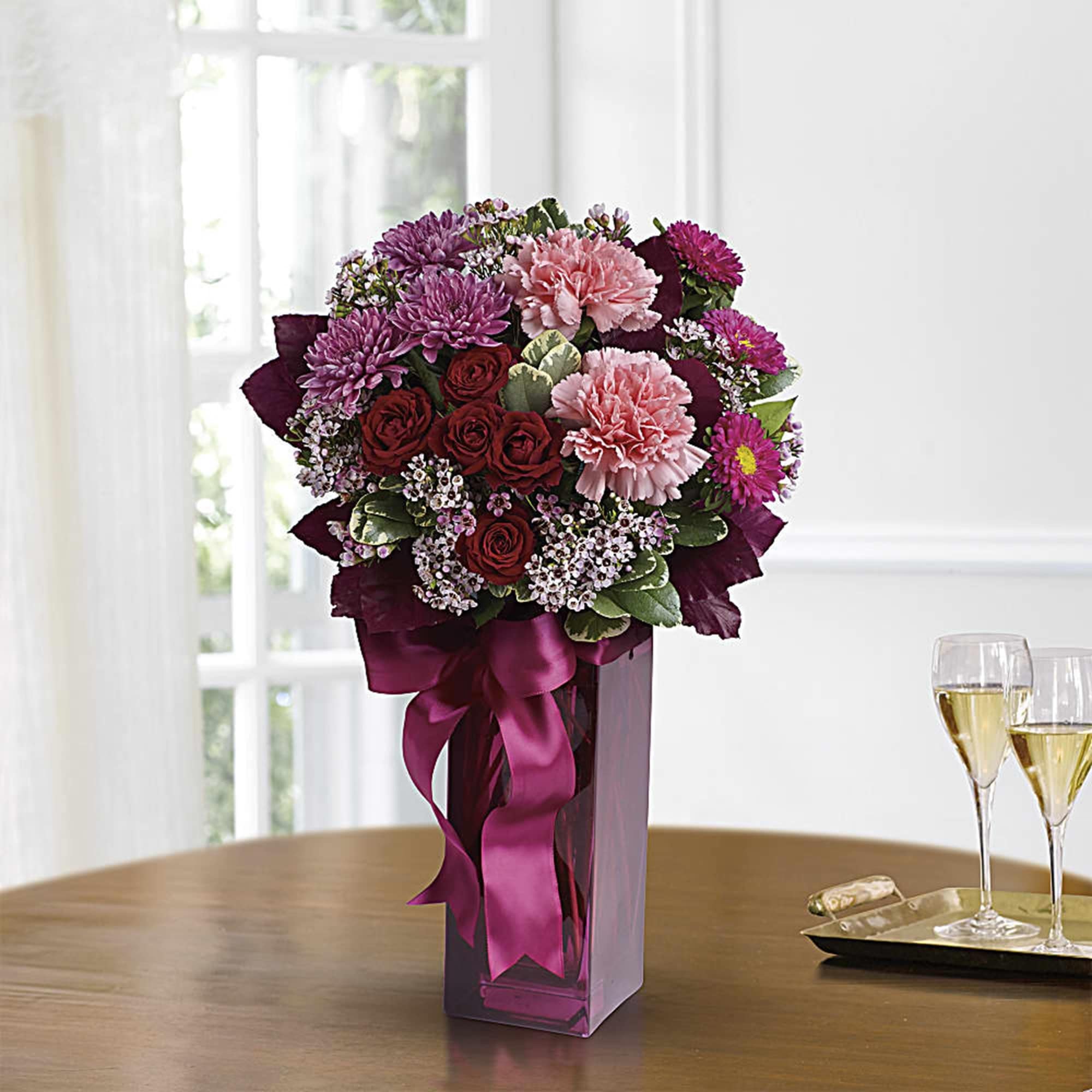 Bouquet of purple, pink, and red flowers in a tall glass vase with a ribbon