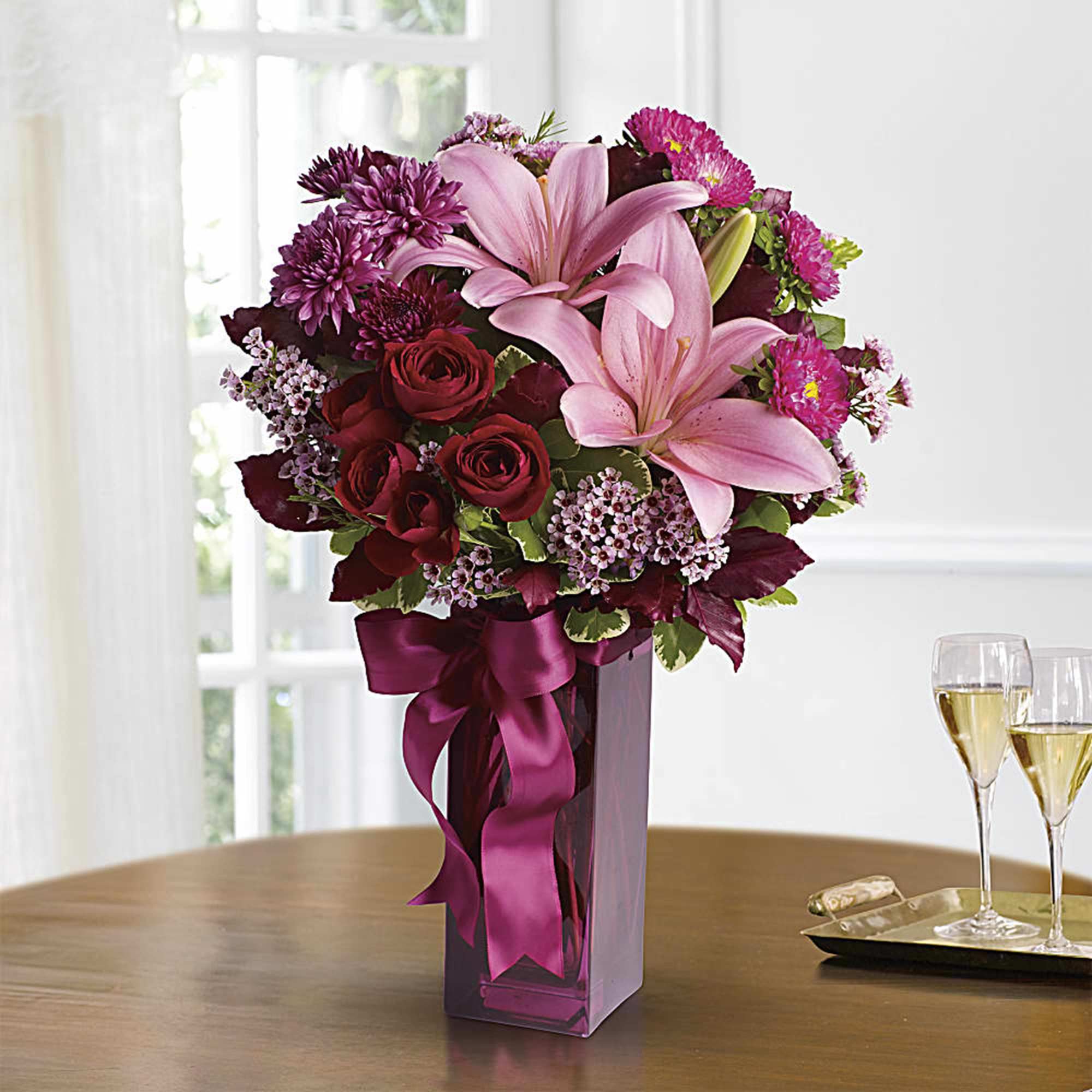 Pink lilies and red roses in a tall purple vase with a ribbon