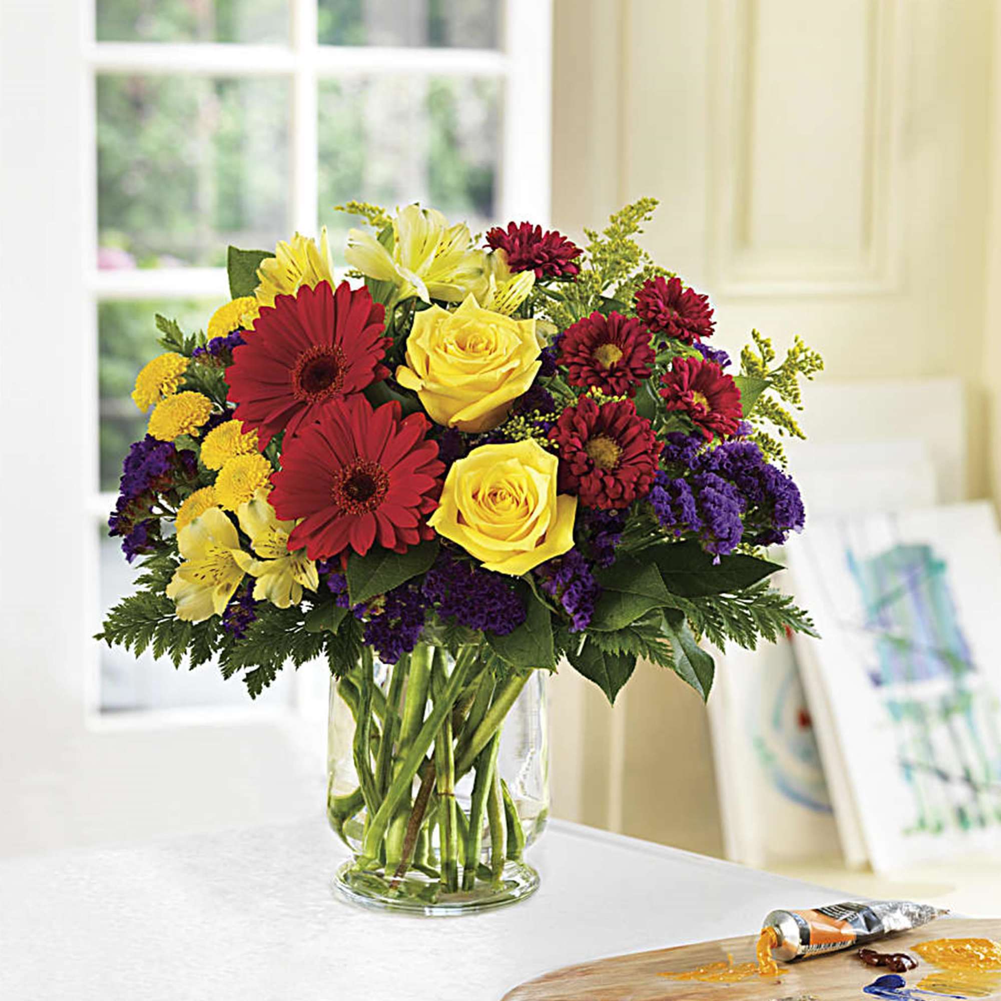 Mixed bouquet of red, yellow, and purple flowers in a clear glass vase