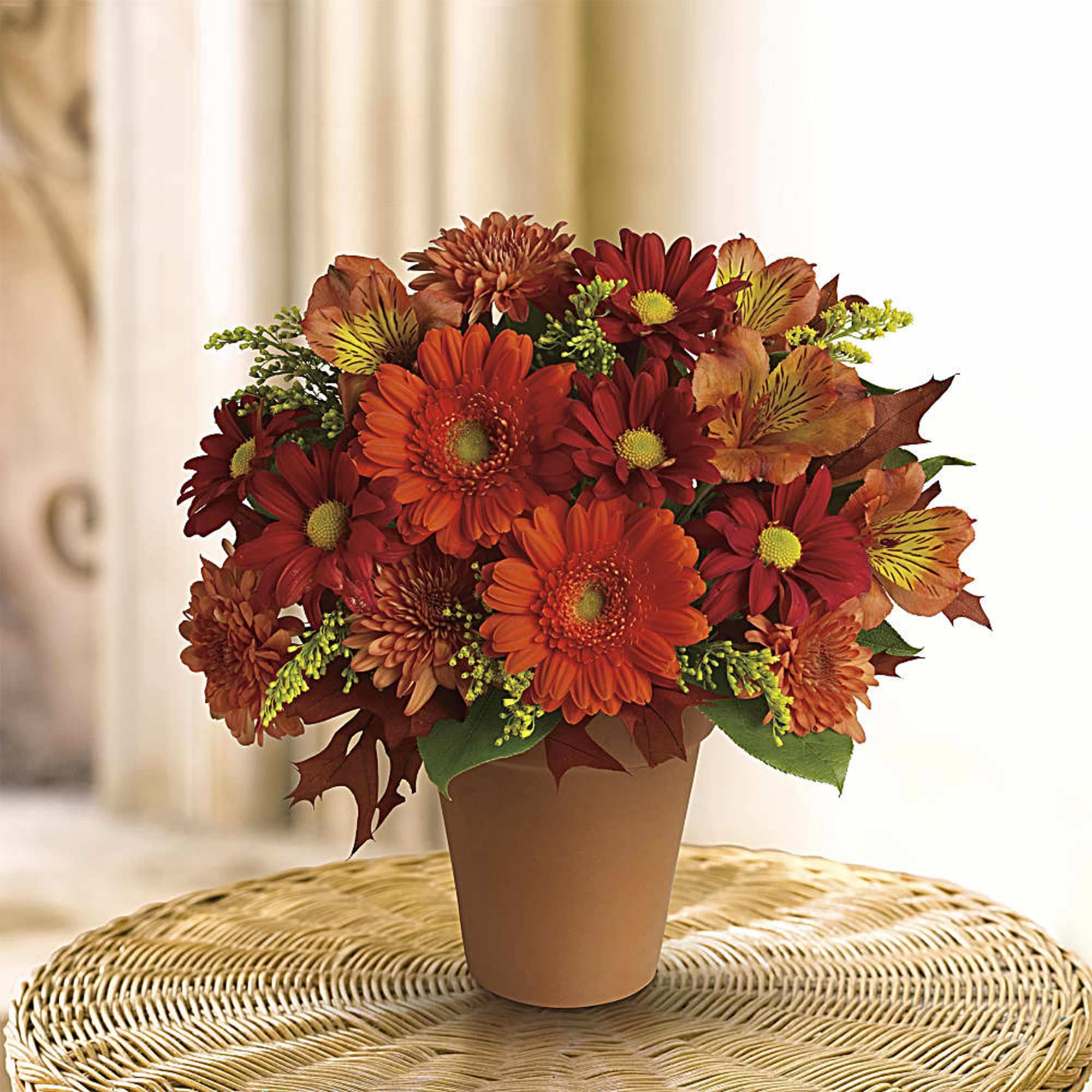 Orange and red flower arrangement in a tan pot